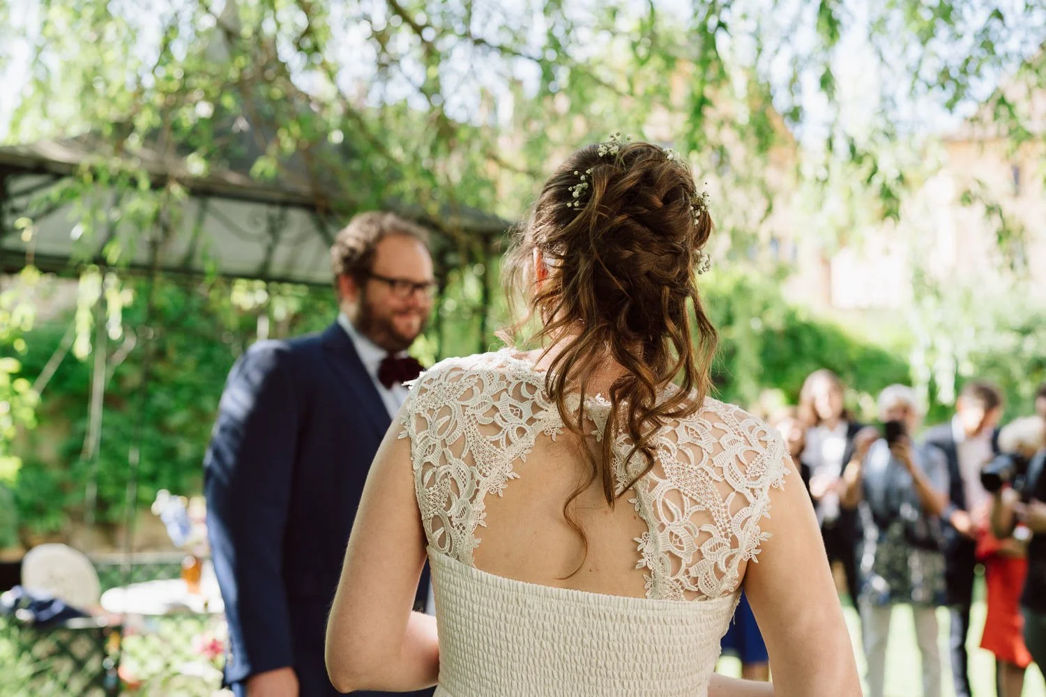 La mariée fait face à son futur époux lors de la cérémonie laïque au Jardin Baillival à Romainmôtier, un instant intime et chargé d’émotion sous les feuillages, Nonante Émotions.