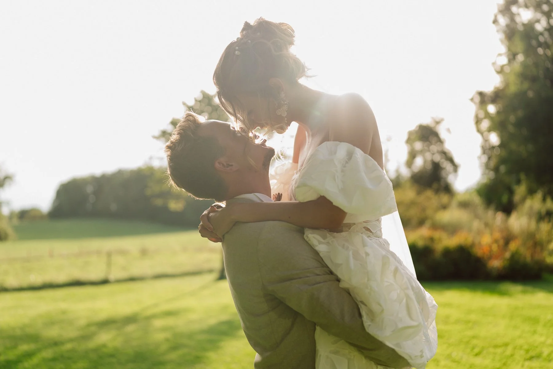 Couple de mariés enlacés dans un jardin au coucher du soleil, lumière dorée en contre-jour, moment intime et tendre lors d’un mariage photographié par Nonante Émotions