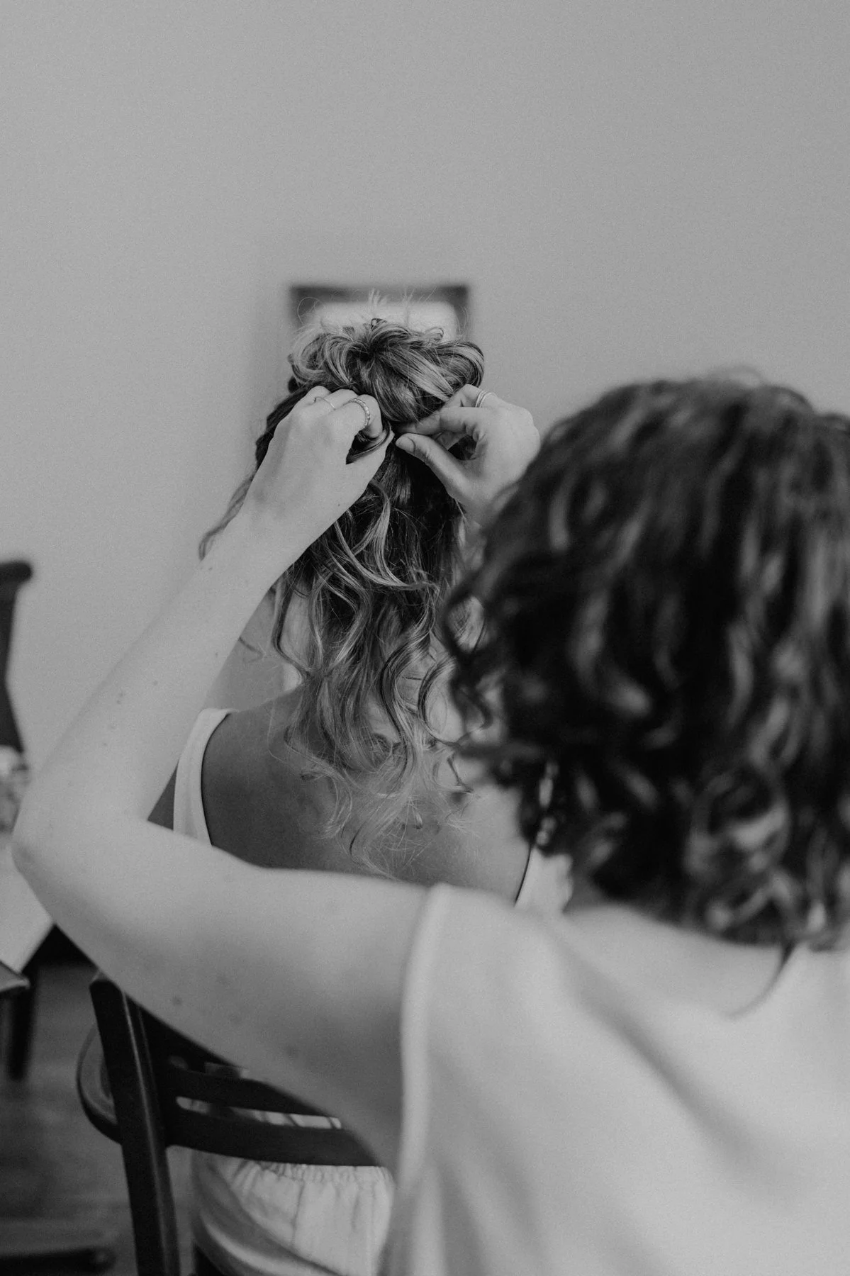 Préparatifs de la mariée, coiffure réalisée par une proche, moment intime en noir et blanc avant le mariage