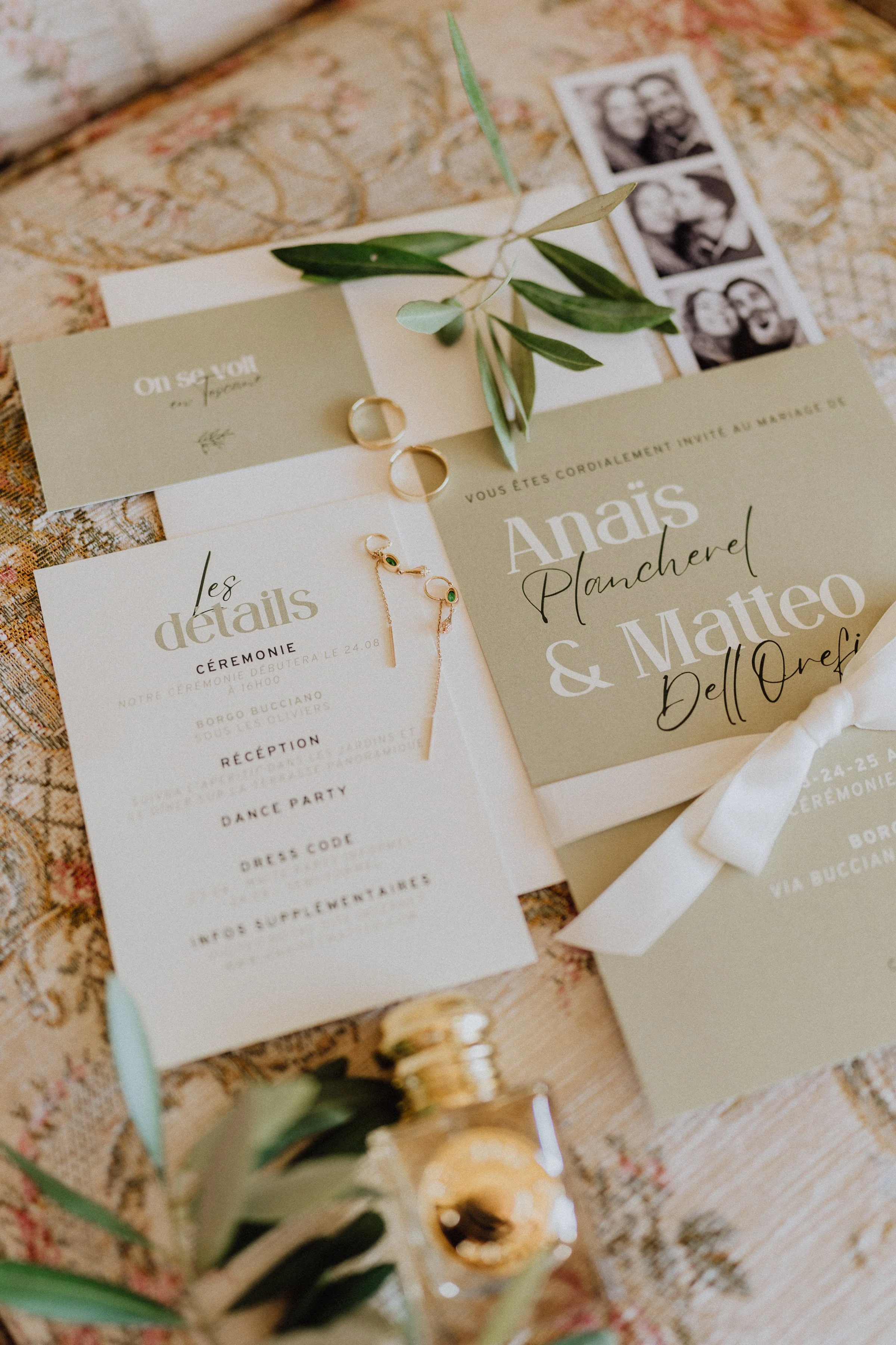 Un flatlay raffiné mettant en avant le faire-part de mariage d'Anaïs Plancherel et Matteo Dell'Orefice. Les tons doux et naturels de la papeterie se marient harmonieusement avec des éléments tels que des feuilles d'olivier, des alliances dorées, et u