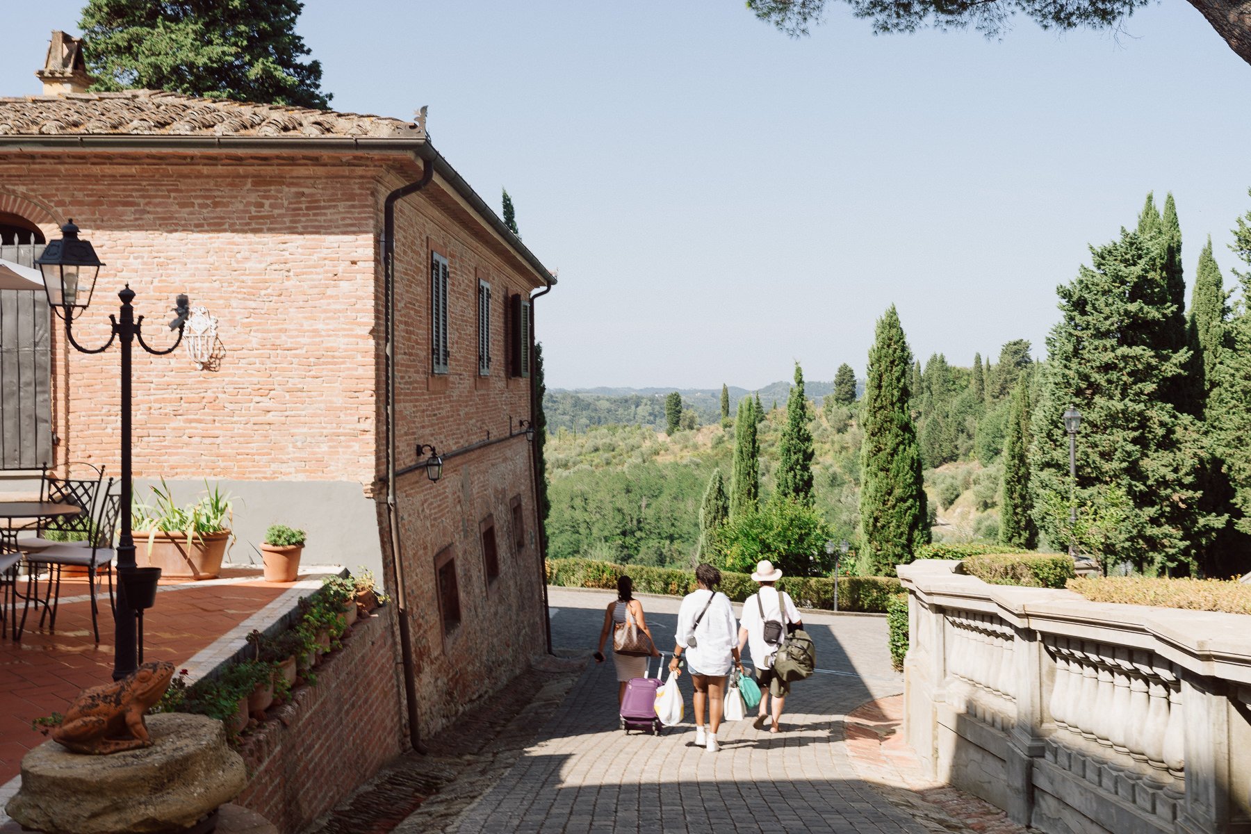Invités quittent le domaine en Toscane, entouré de collines, cyprès et bâtisses en pierre sous le soleil italien