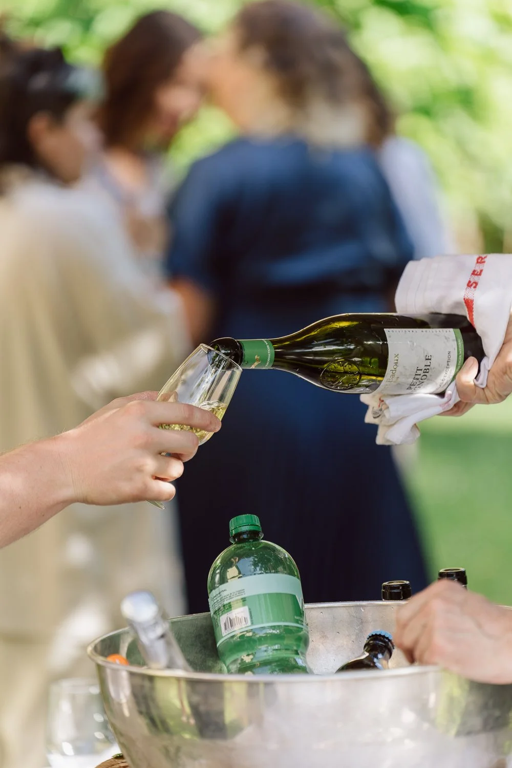 Service de champagne lors du cocktail de mariage au Jardin Baillival à Romainmôtier, bouteille versée dans une flûte, ambiance conviviale en extérieur, photo par Nonante Émotions.