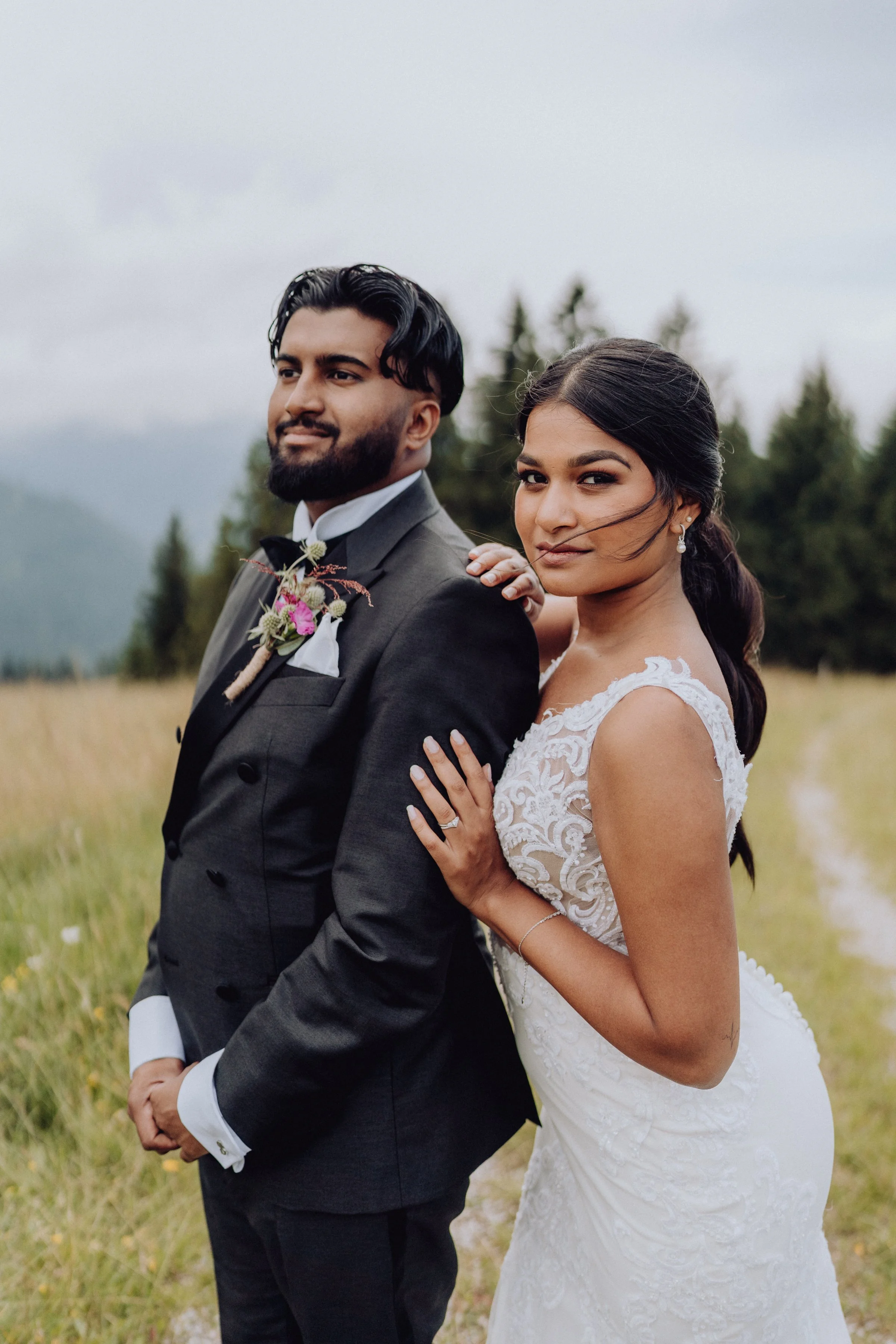 Un couple de mariés posé devant un paysage de montagne. La mariée porte une robe en dentelle ajustée, et le marié, un costume classique. L’atmosphère naturelle et sereine renforce la beauté de leur union.