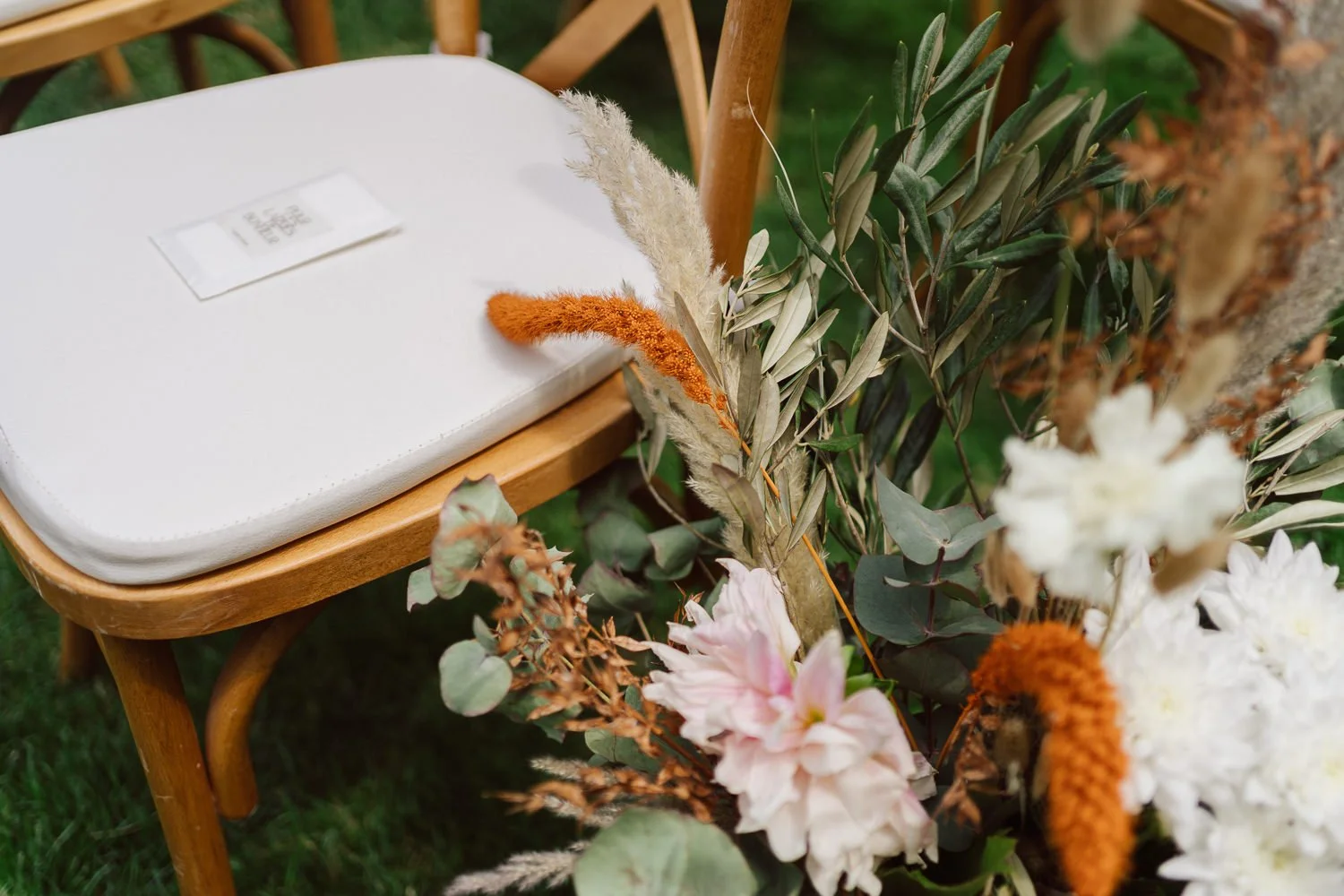 Chaise de cérémonie en bois avec assise blanche, décorée de fleurs séchées et feuillages dans un esprit naturel et élégant lors d’un mariage en extérieur, photo par Nonante Émotions