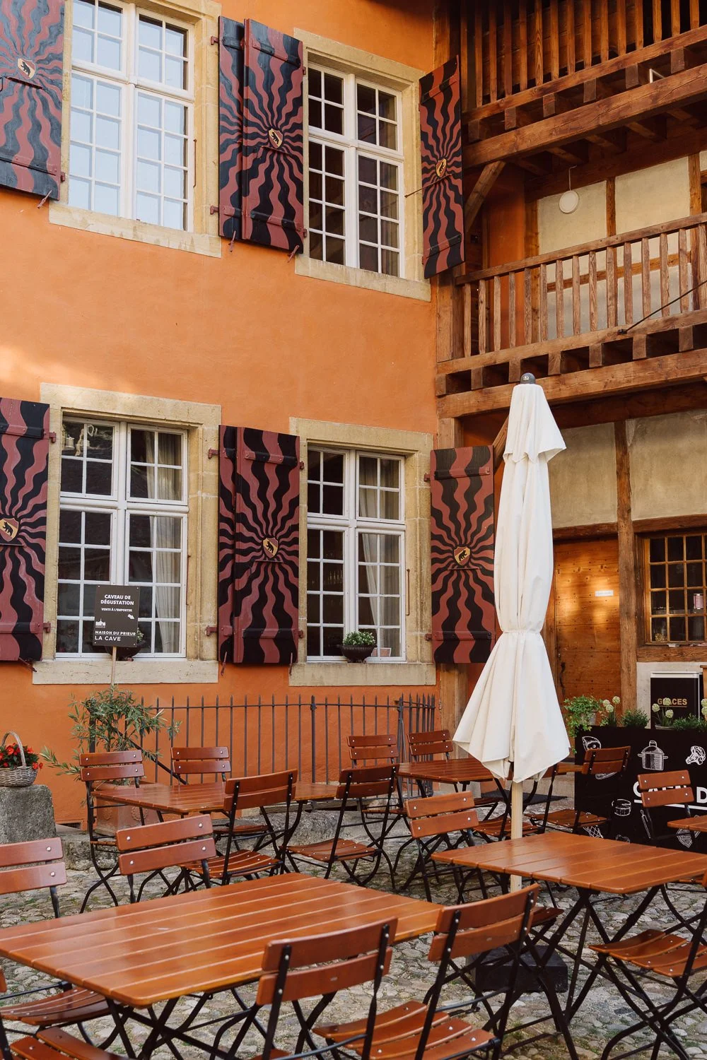 Terrasse de la Maison Du Prieur à Romainmôtier, tables en bois dans une cour intérieure aux façades colorées et volets décorés, lieu de réception de mariage au charme authentique, photo par Nonante Émotions.