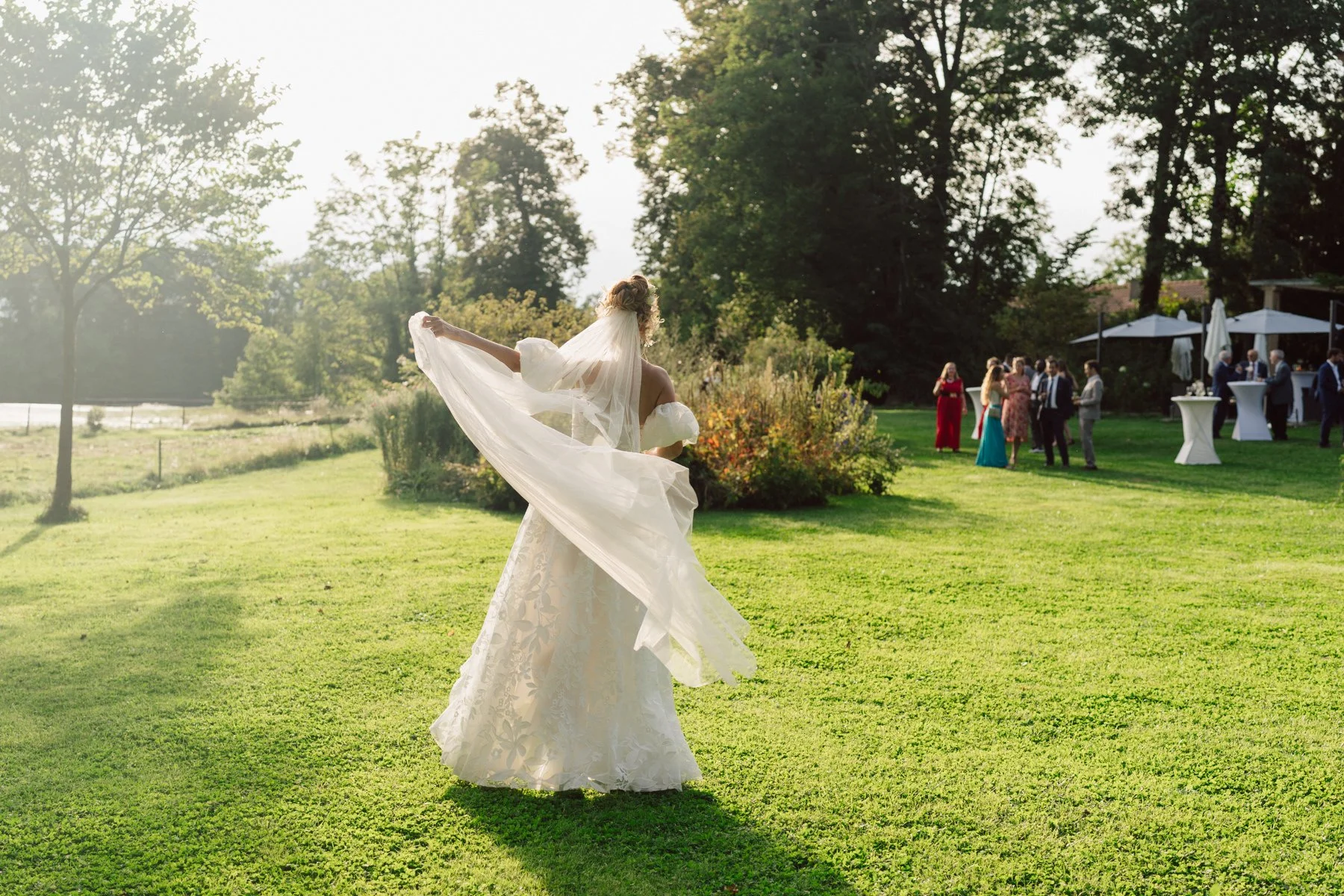 Silhouette de la mariée dans le parc du Castel de Bois-Genoud, voile au vent et ambiance douce de fin de journée