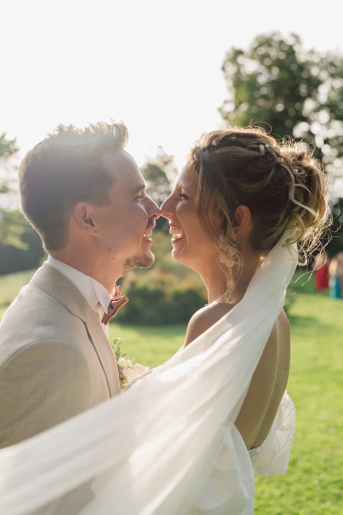 Portrait intime des mariés se souriant face à face, baignés de lumière, lors de leur mariage au Castel de Bois-Genoud
