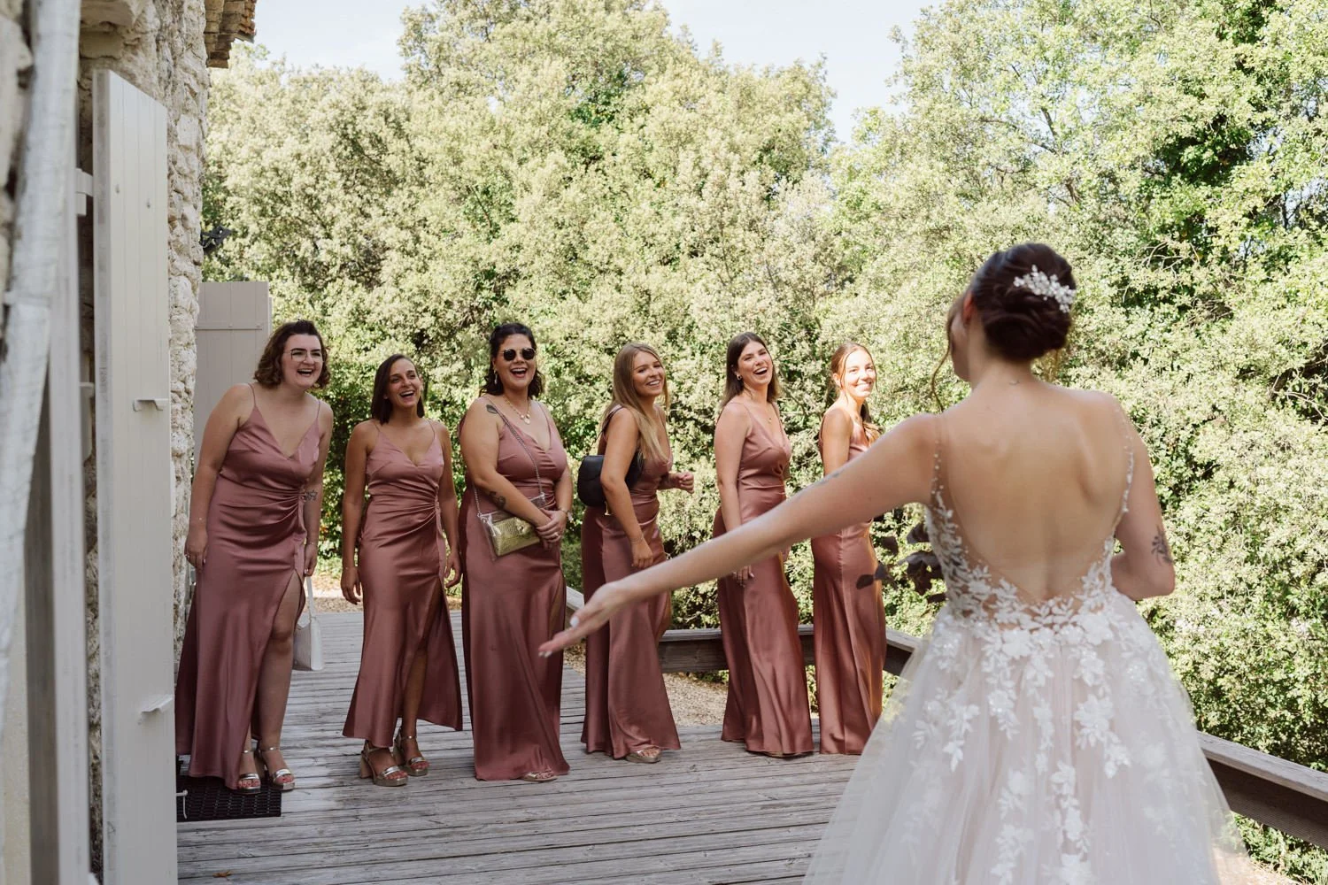 La mariée découvre ses demoiselles d’honneur en robes terracotta sur une terrasse en bois au Domaine de Sarson, entourées de verdure en Provence.