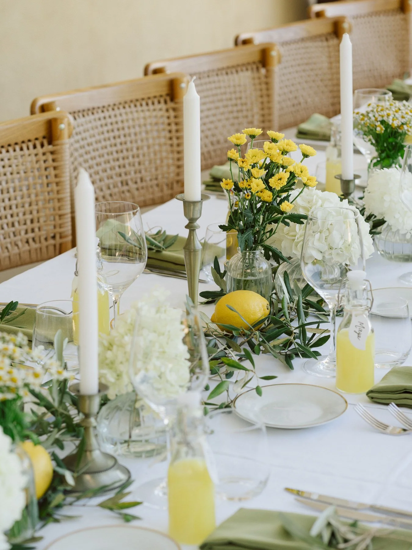 Décoration de table de mariage élégante avec citrons, feuillage d’olivier, fleurs blanches et jaunes, bougies et serviettes vert olive, ambiance méditerranéenne raffinée.