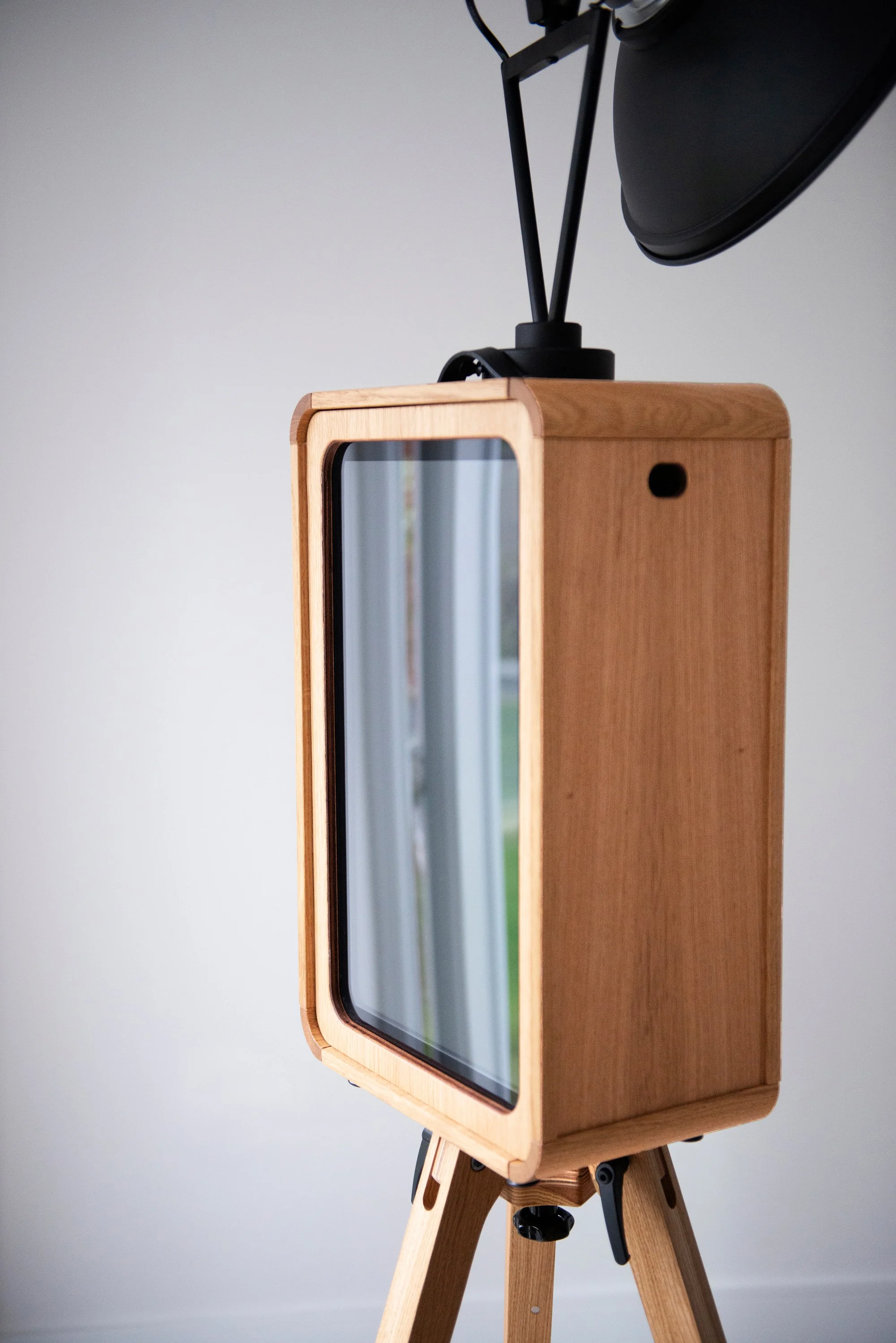 Photographie d'un appareil photo sur un trépied en bois, avec un boîtier en bois naturel et un grand écran à l'avant.