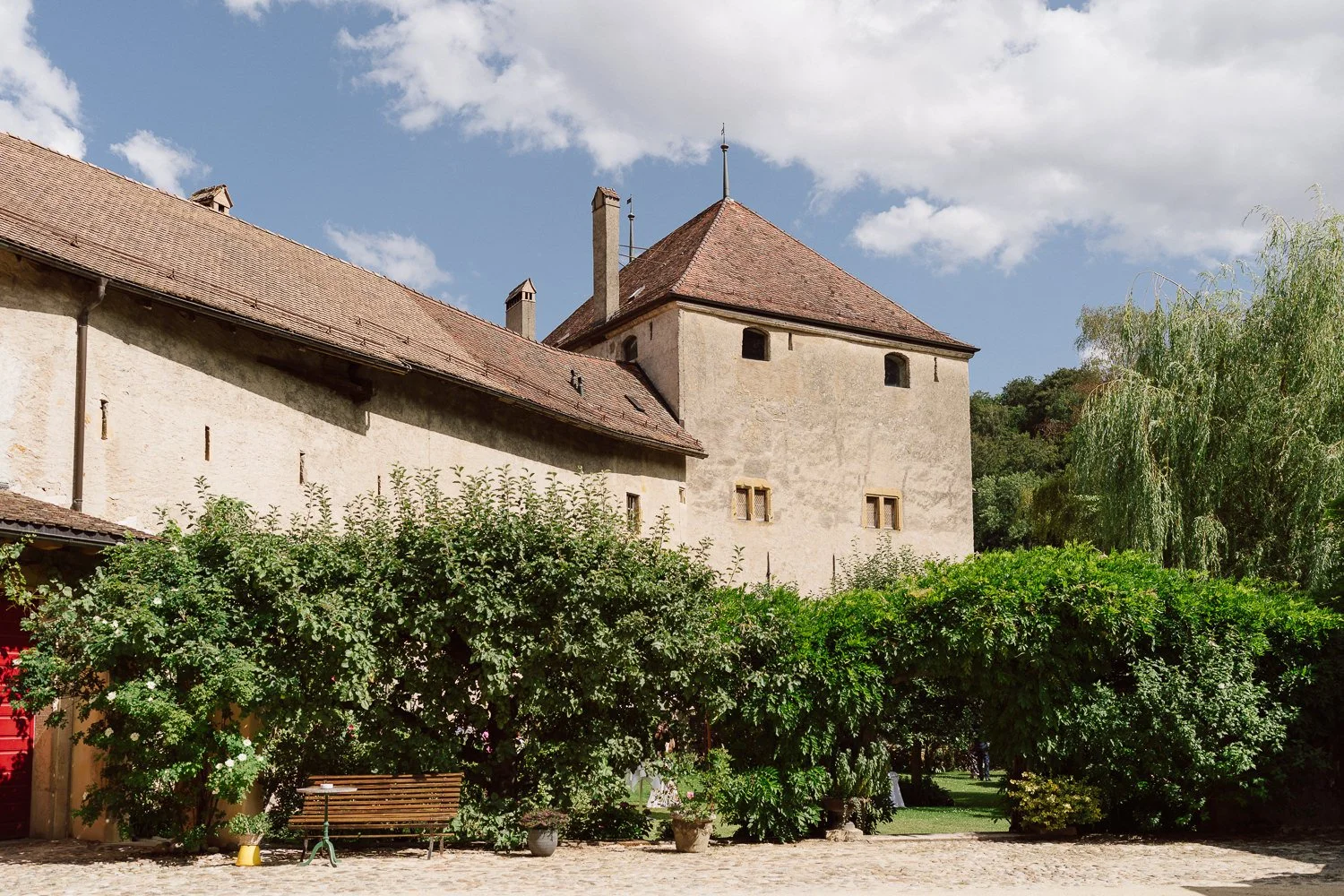Vue extérieure du Jardin Baillival à Romainmôtier, bâtiments historiques entourés de verdure, lieu de réception de mariage au charme authentique en Suisse, photo par Nonante Émotions.