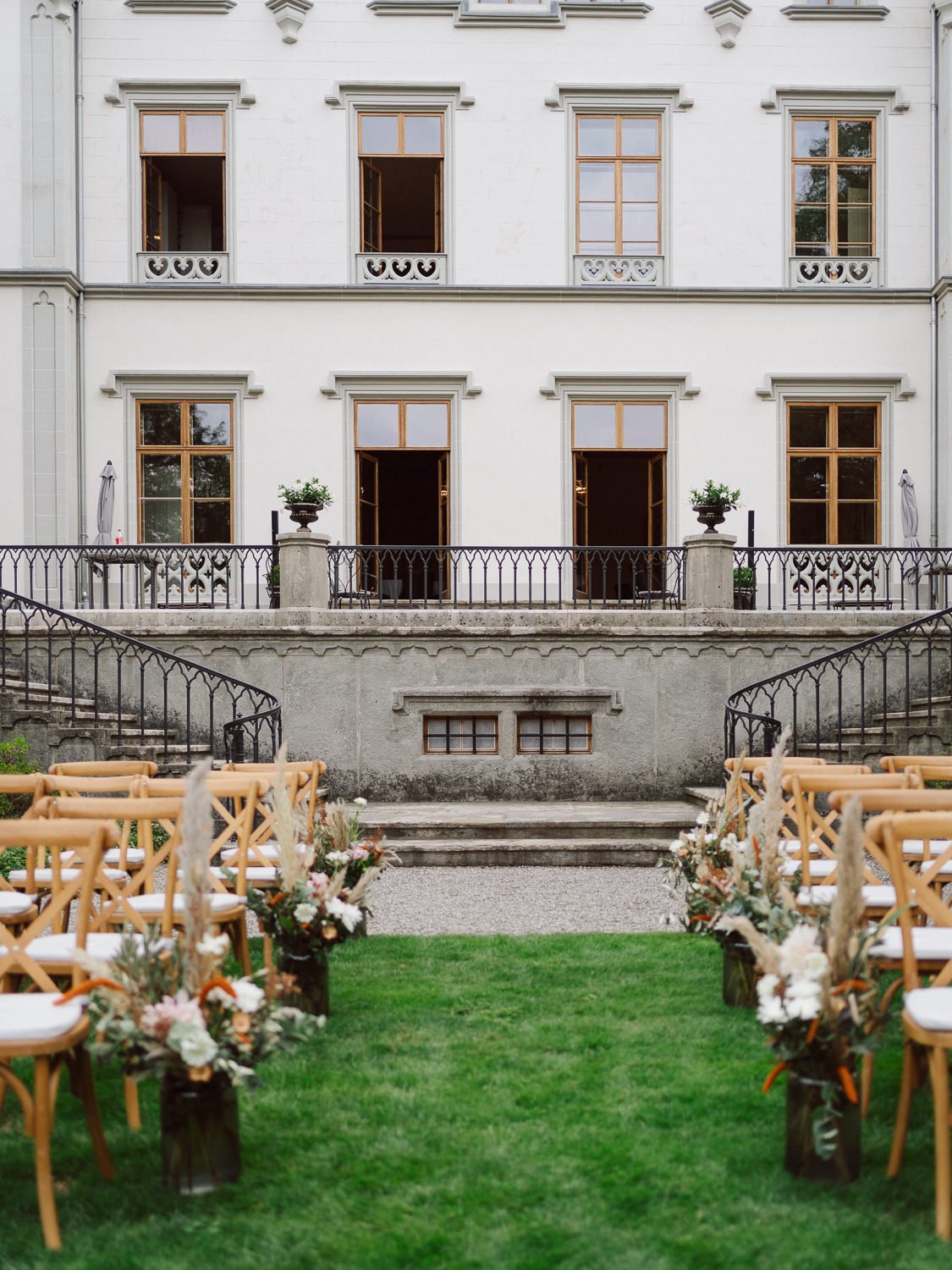Allée de cérémonie laïque en extérieur au Château de l’Aile à Vevey, avec chaises en bois et décorations florales naturelles devant la façade du château, photo de mariage par Nonante Émotions