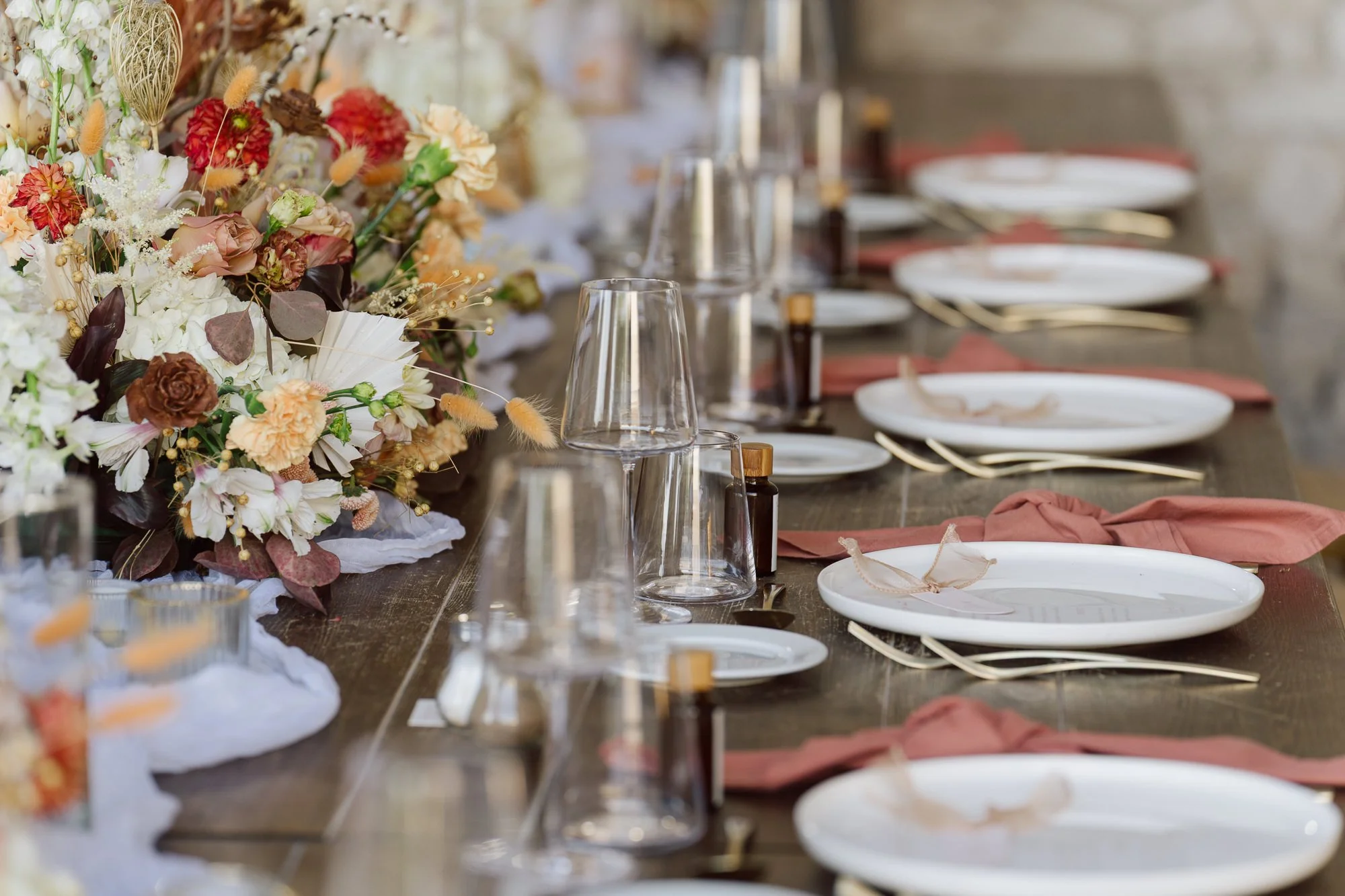 Détail de décoration de table de mariage avec composition florale, vaisselle blanche et verres élégants dans un cadre en pierre en Provence.