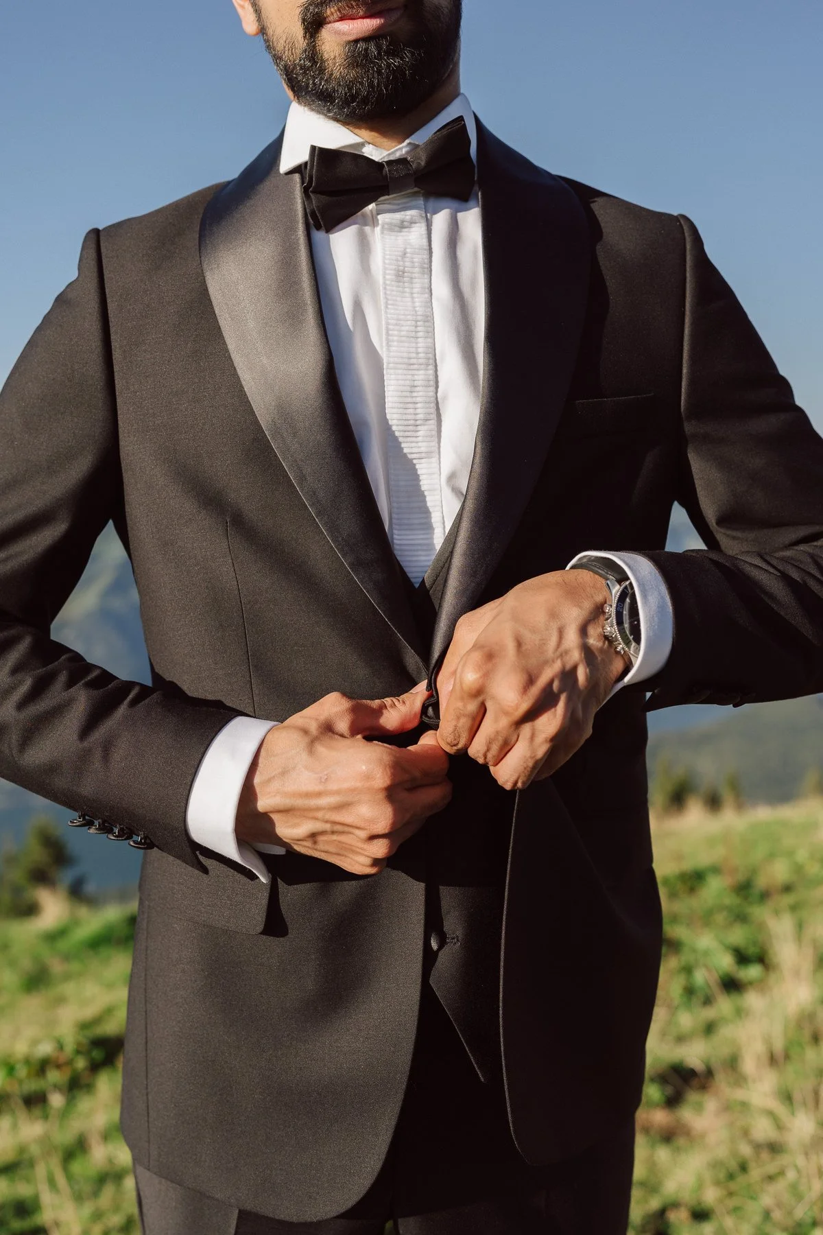Marié en costume noir ajustant sa veste et son nœud papillon en montagne en Suisse – photo de préparatifs mariage par Nonante Émotions