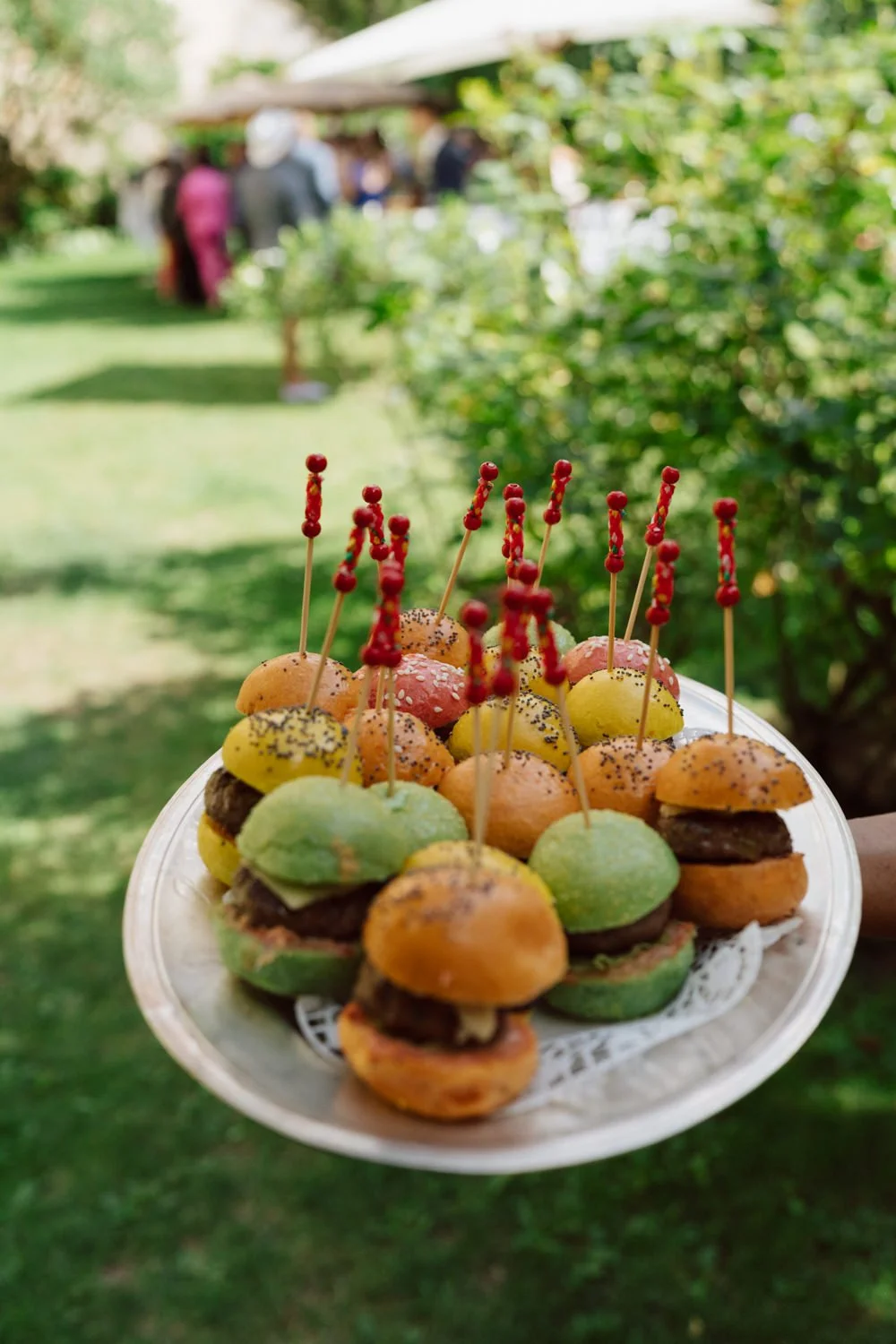 Plateau de mini burgers colorés servis lors du cocktail de mariage au Jardin Baillival, ambiance estivale dans le jardin.