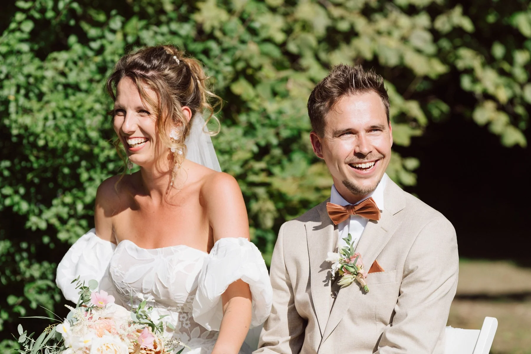 Les mariés sourient et rient pendant la cérémonie laïque en extérieur au Castel de Bois-Genoud, baignés de lumière naturelle