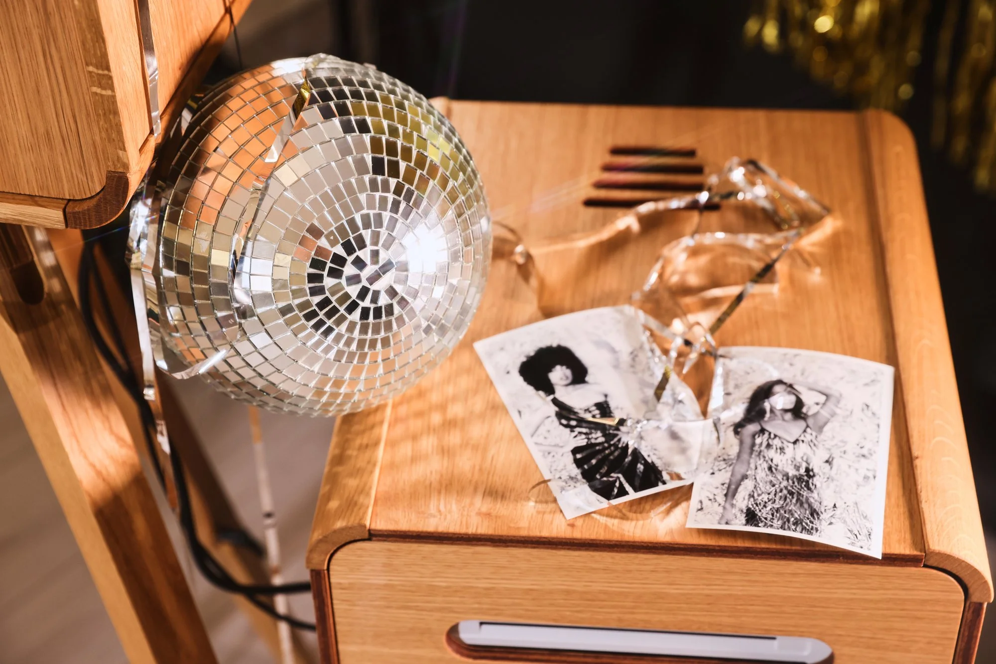 Une boule disco miroir, des photos en noir et blanc et un objet en forme de diamant en verre reposent sur une table en bois.
