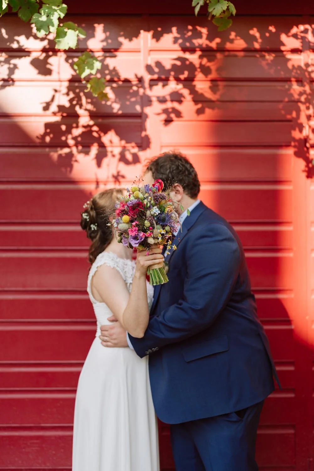 Portrait des mariés s’embrassant derrière le bouquet, ambiance graphique et colorée.