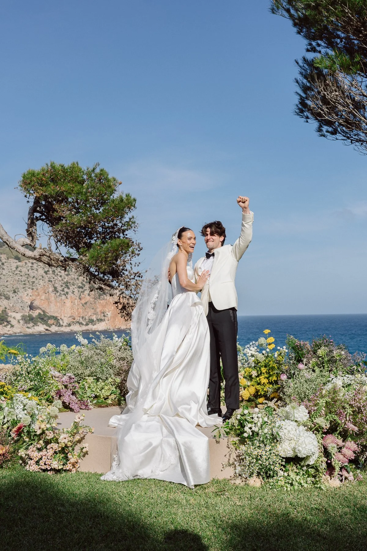 Bride and groom celebrating during a seaside wedding ceremony in Mallorca, colorful floral design and Mediterranean backdrop creating an elegant luxury destination wedding atmosphere