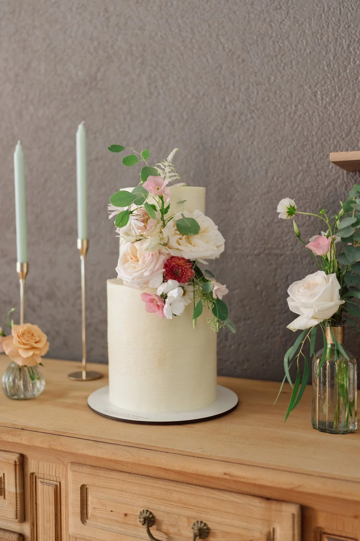 Gâteau de mariage élégant décoré de fleurs, photographié au Castel Bois-Genoud lors du mariage de Diana et Loïc, avec vue sur le lac Léman.