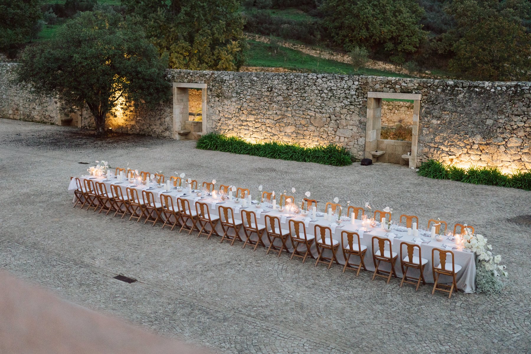 Réception de mariage destination à la Quinta do Pinho au Portugal avec longue table élégante dressée dans la cour en pierre au coucher du soleil