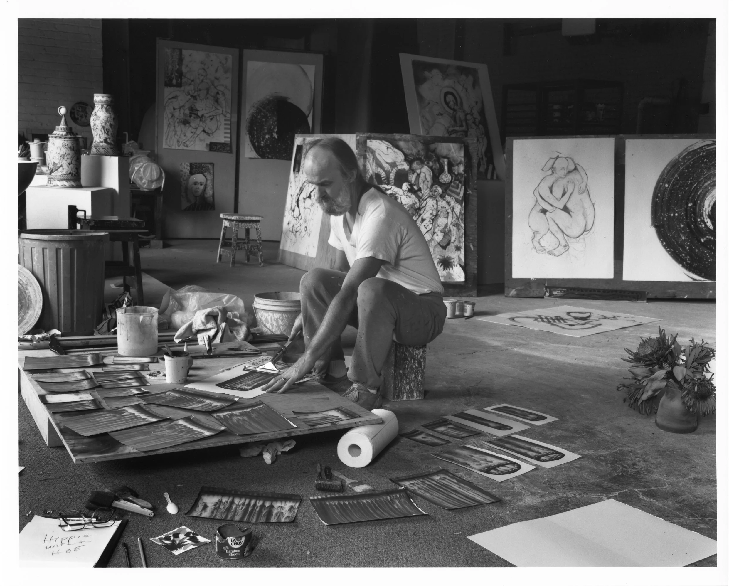 Black and white portrait of an artist Edward Eberle drawing in his studio in 1991 and surrounded by drawings and ceramics sculptures