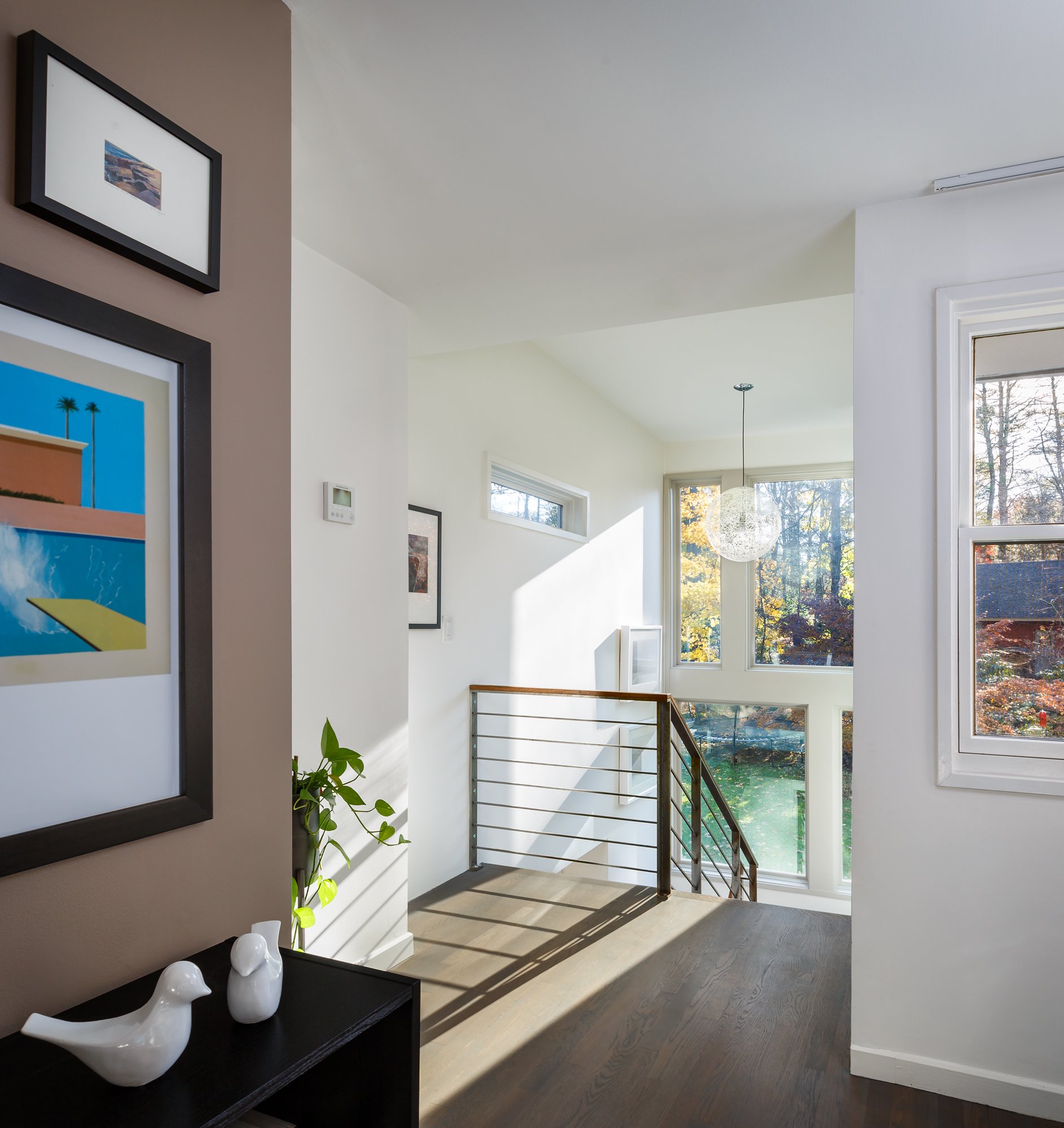 Interior view from the existing second floor looking toward the newly added staircase surrounded by large picture windows that flood the space with natural light. The flat stair tower ceiling is higher than that of the existing second floor and featu