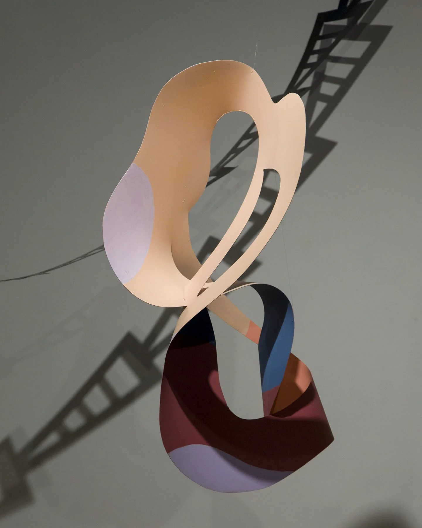 Abstract hanging sculpture with curved, ribbon-like elements casting shadows on the ceiling.