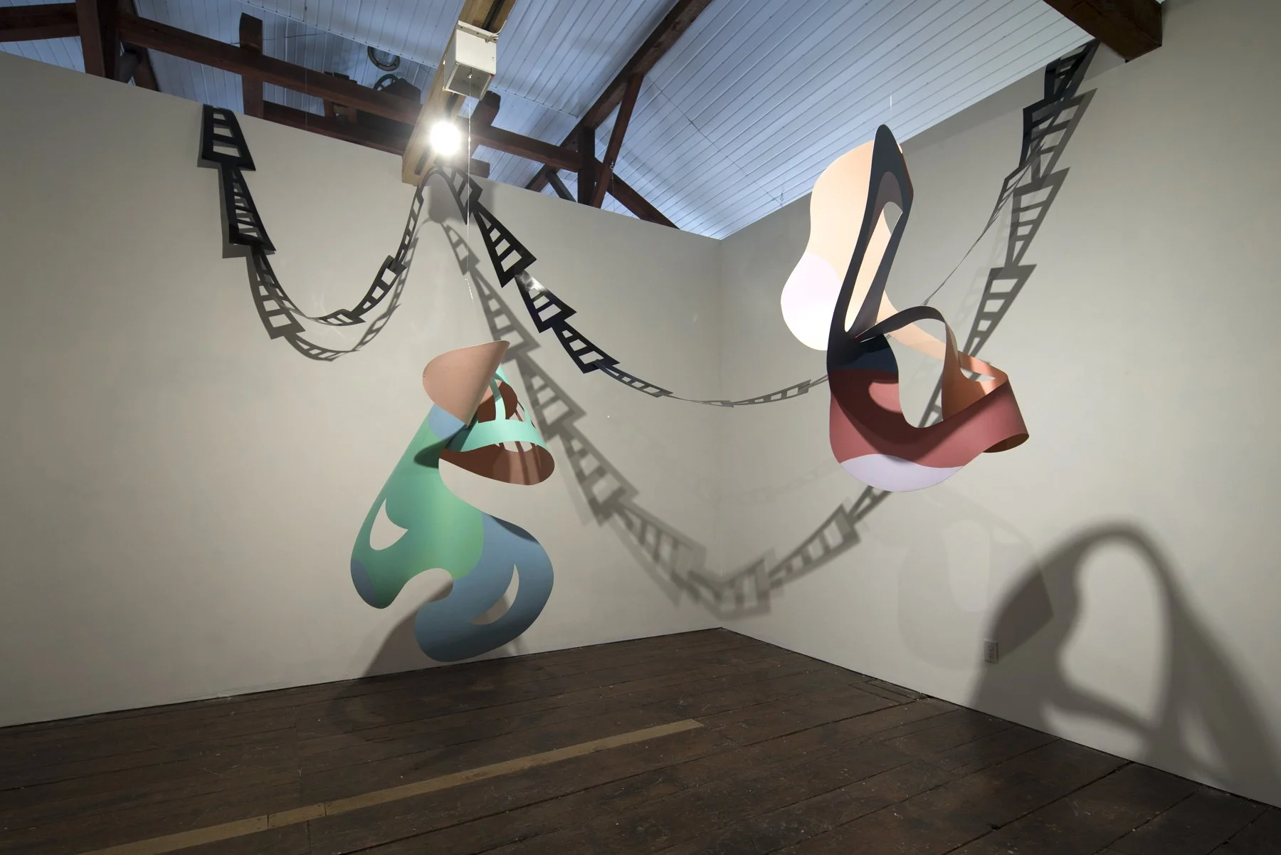 Colorful abstract sculptures of a shoe and a handbag with shadow art and film strip patterns on the wall