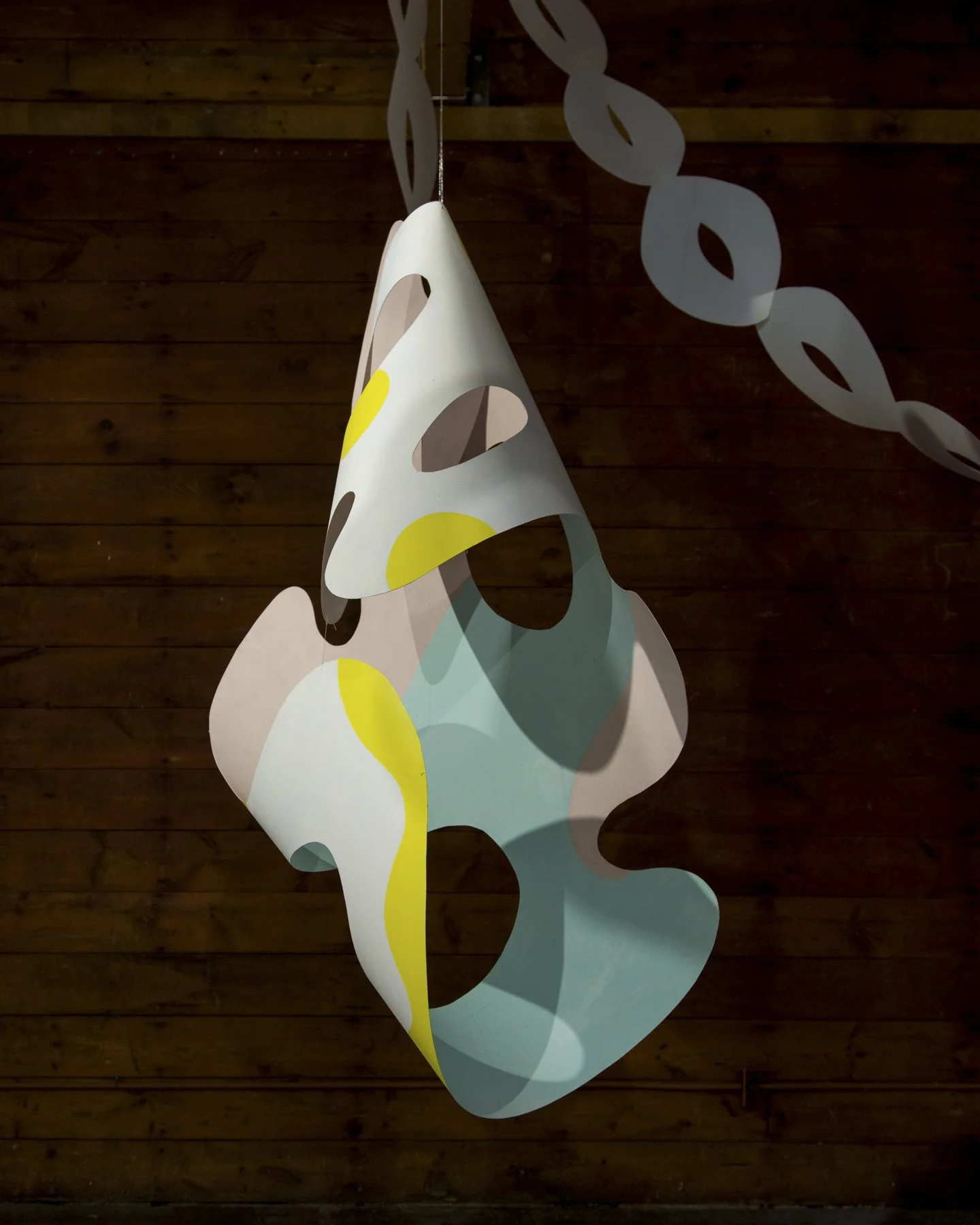 Colorful, modern pendant light fixture with abstract design, hanging against a wooden wall.