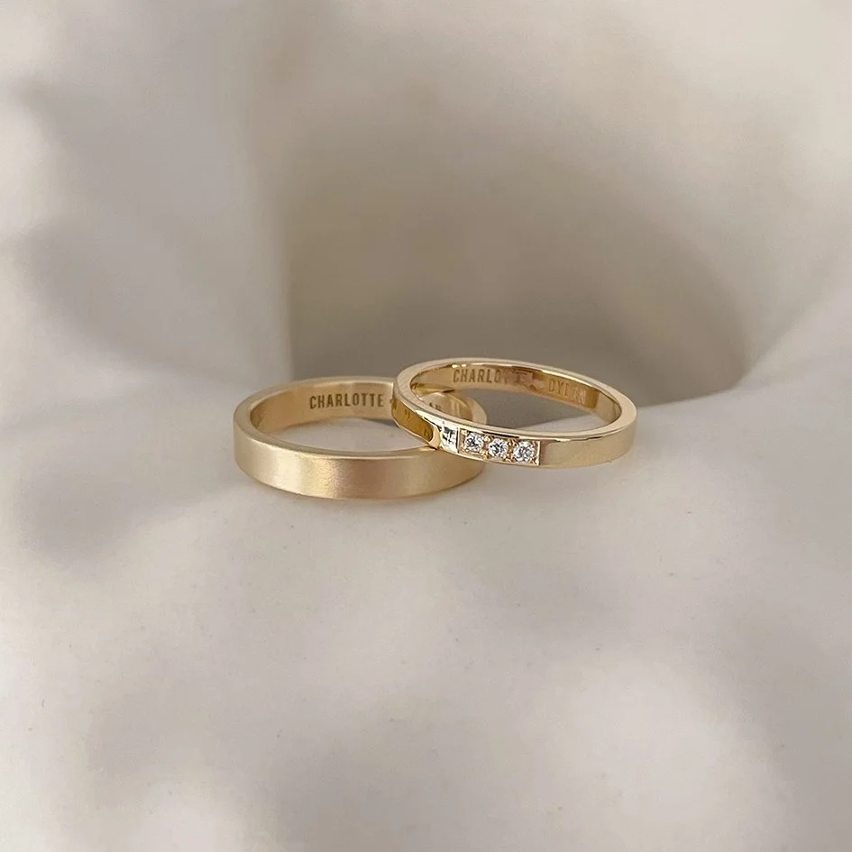 A pair of handmade, minimalist wedding bands made from recycled gold, with the women’s band featuring three lab-grown diamonds