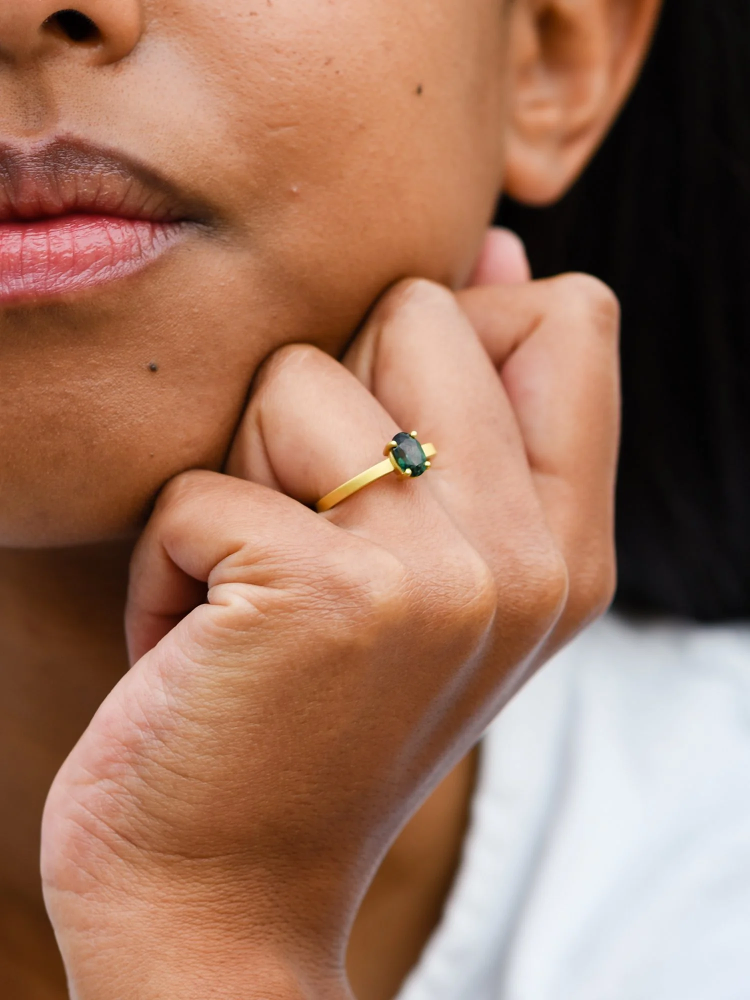 Model wearing an oval engagement ring in Antwerp. In yellow gold with green gemstone.