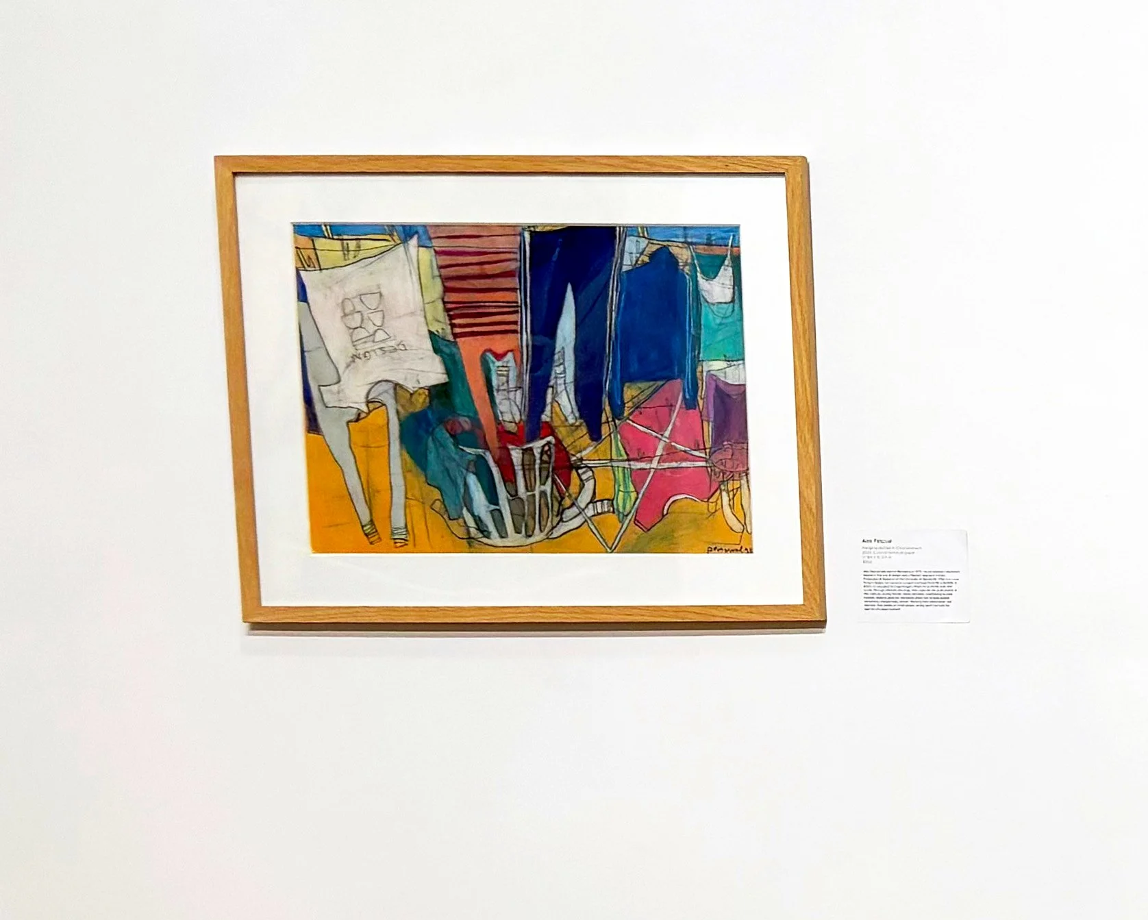 Colorful abstract artwork featuring geometric shapes and undefined figures, framed and displayed on a white gallery wall.