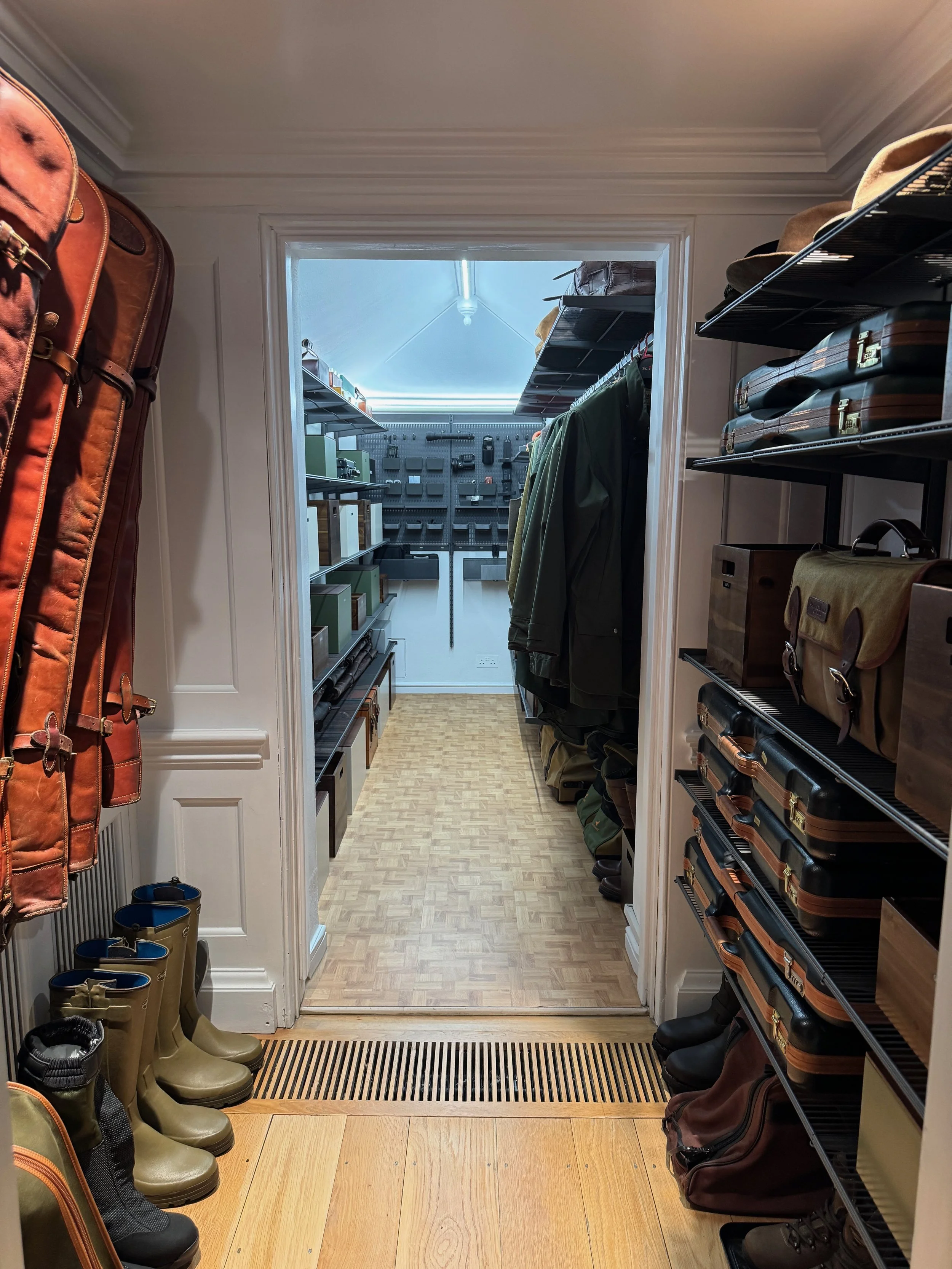 A boot room with gun slips, wellington boots, tweed jackets and organised shelving