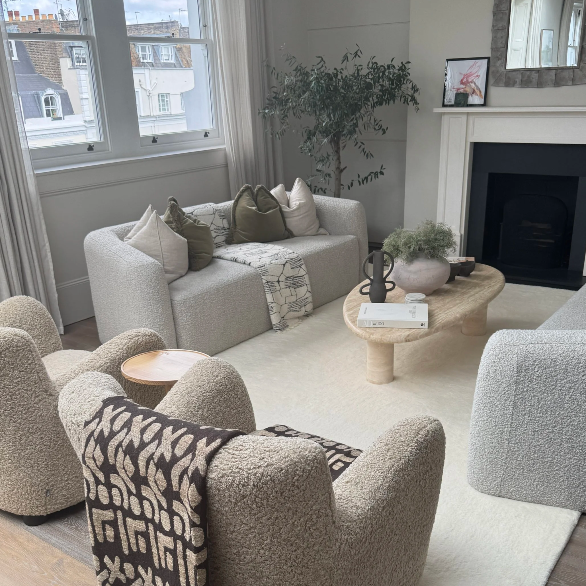 Living room area with neutral tone armshairs and coffee table, fireplace and olive tree