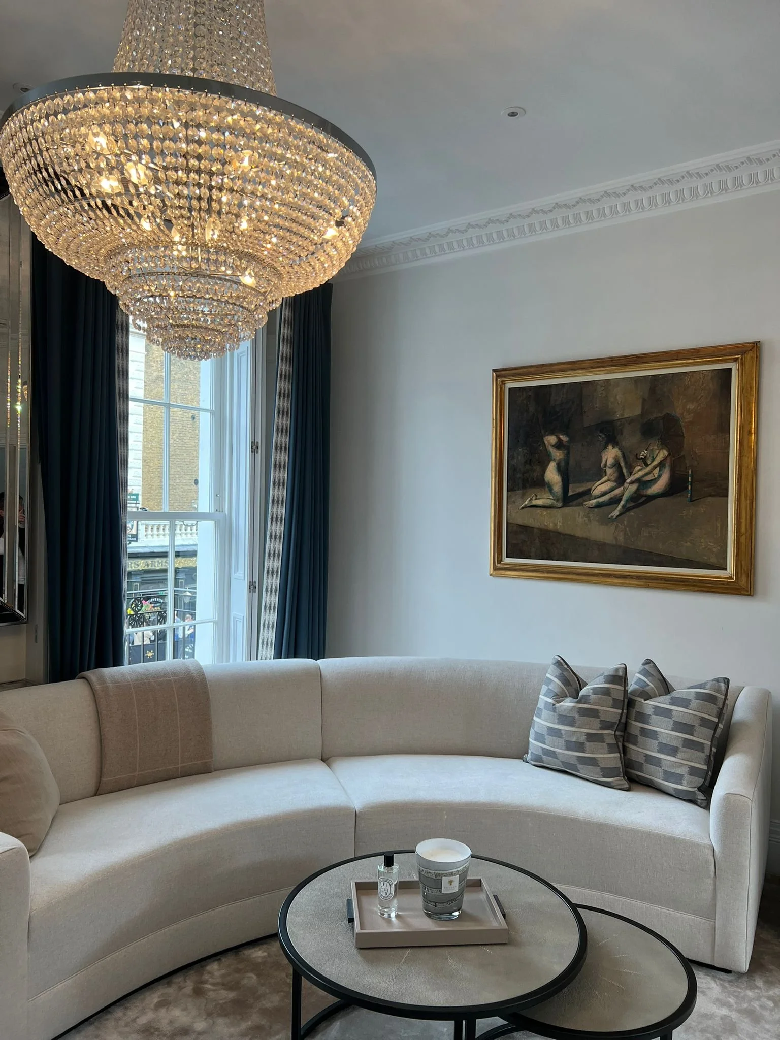 A living room with cream sofa, chandelier, blue curtains and large sash window
