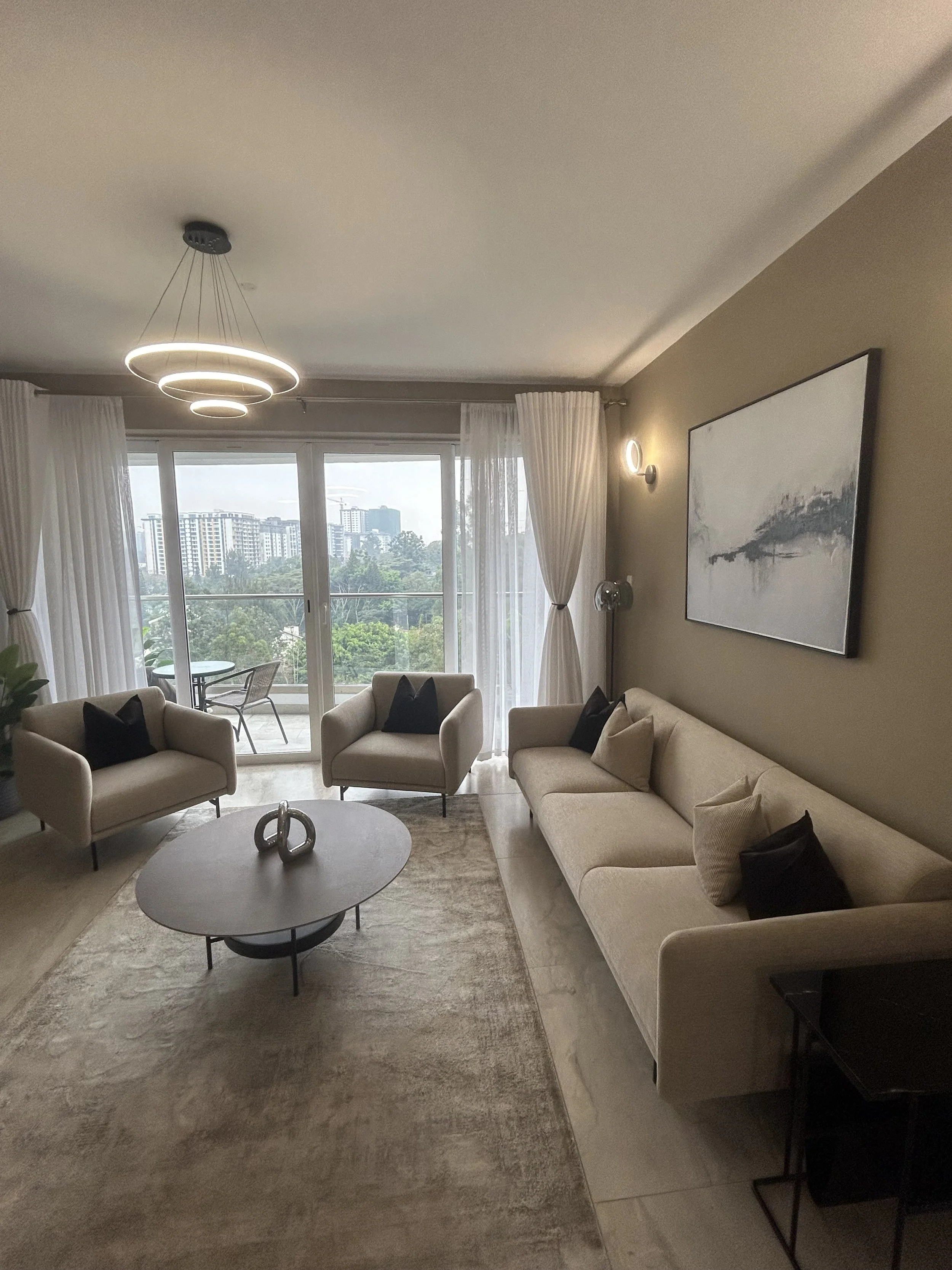 Living room space with sofa, two armchairs and coffee table. Decorative silver object and grey rug. Modern pendant light