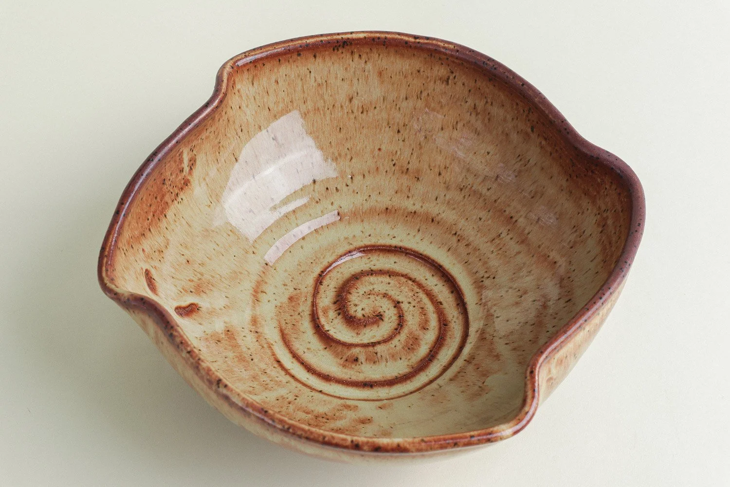 Handmade studio pottery bowl featuring a rustic, earthy-glazed swirl interior and a scalloped rim.