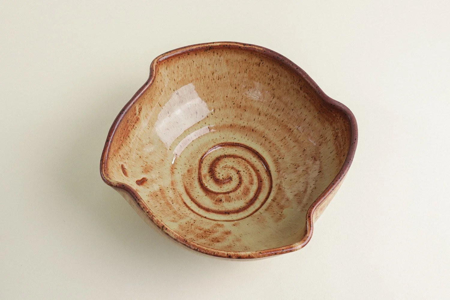 Handmade studio pottery bowl featuring a rustic, earthy-glazed swirl interior and a scalloped rim.