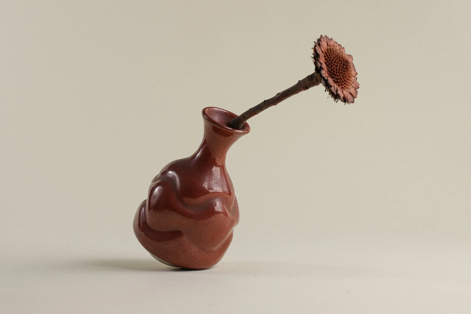 Handmade studio pottery bud vase featuring an organic, flowing form and reddish-brown glaze.