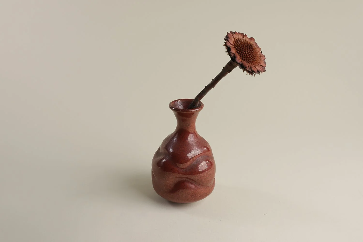 Handmade studio pottery bud vase featuring an organic, flowing form and reddish-brown glaze.