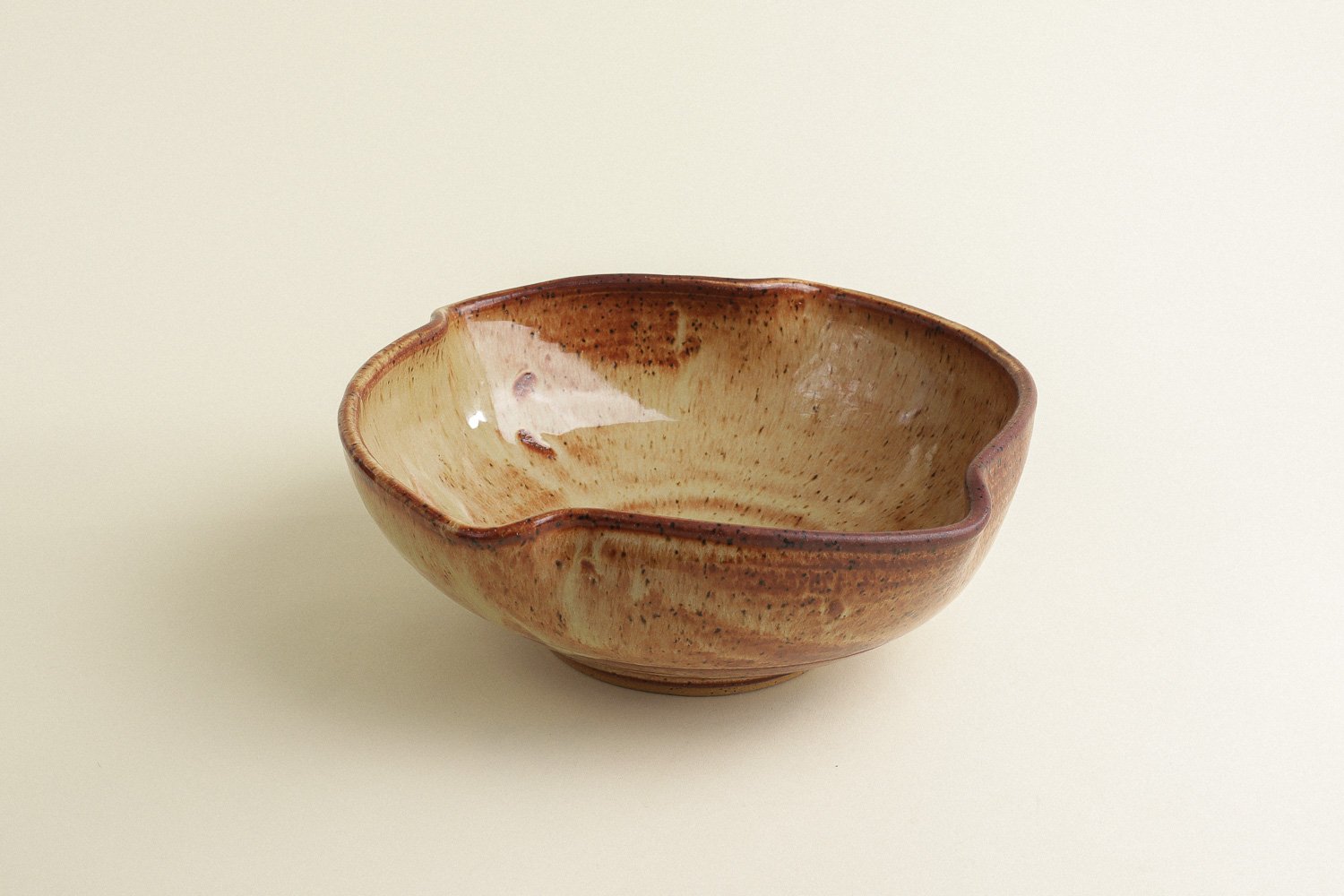 Handmade studio pottery bowl featuring a rustic, earthy-glazed swirl interior and a scalloped rim.