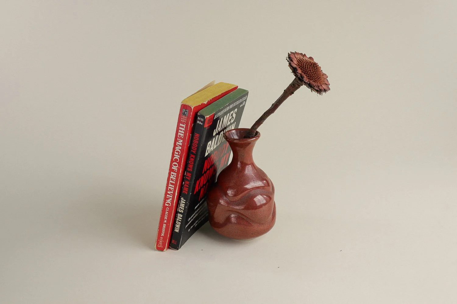 Handmade studio pottery bud vase featuring an organic, flowing form and reddish-brown glaze.