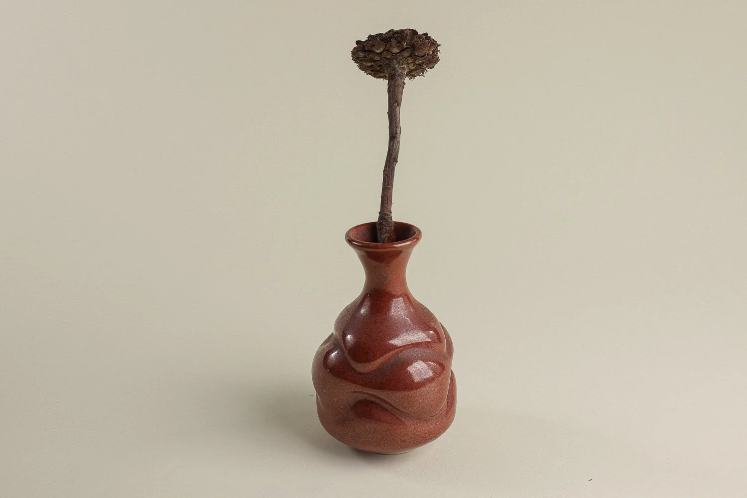 Handmade studio pottery bud vase featuring an organic, flowing form and reddish-brown glaze.
