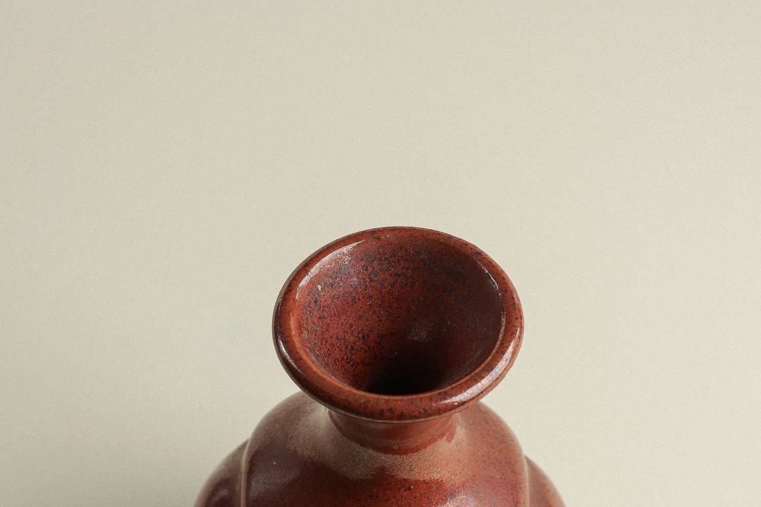 Handmade studio pottery bud vase featuring an organic, flowing form and reddish-brown glaze.