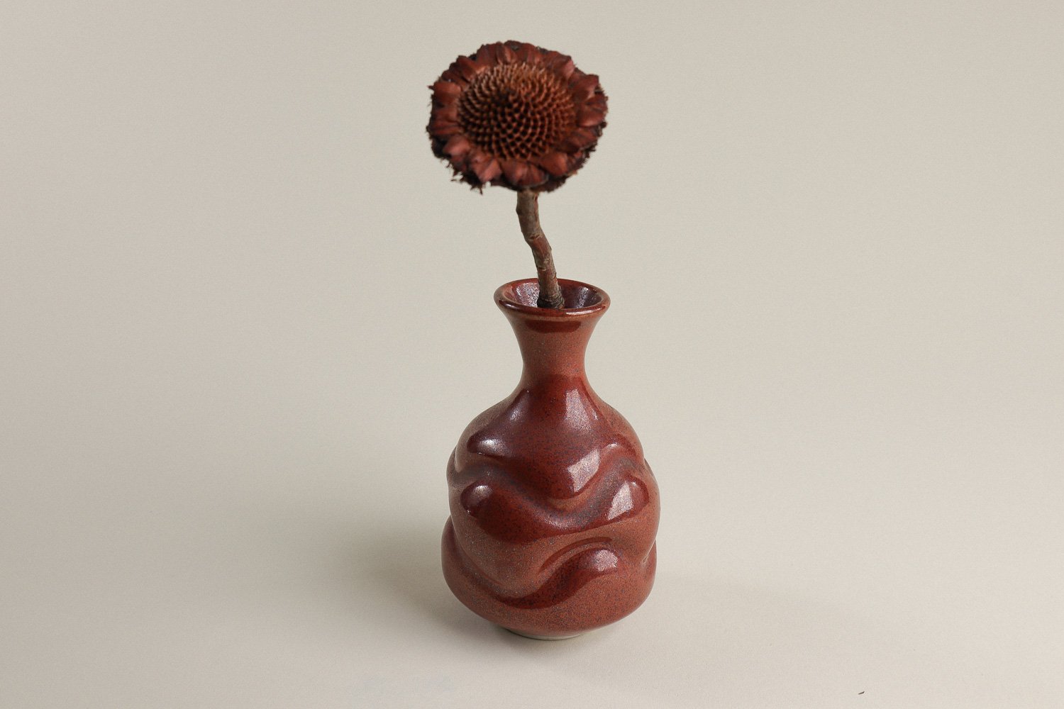 Handmade studio pottery bud vase featuring an organic, flowing form and reddish-brown glaze.
