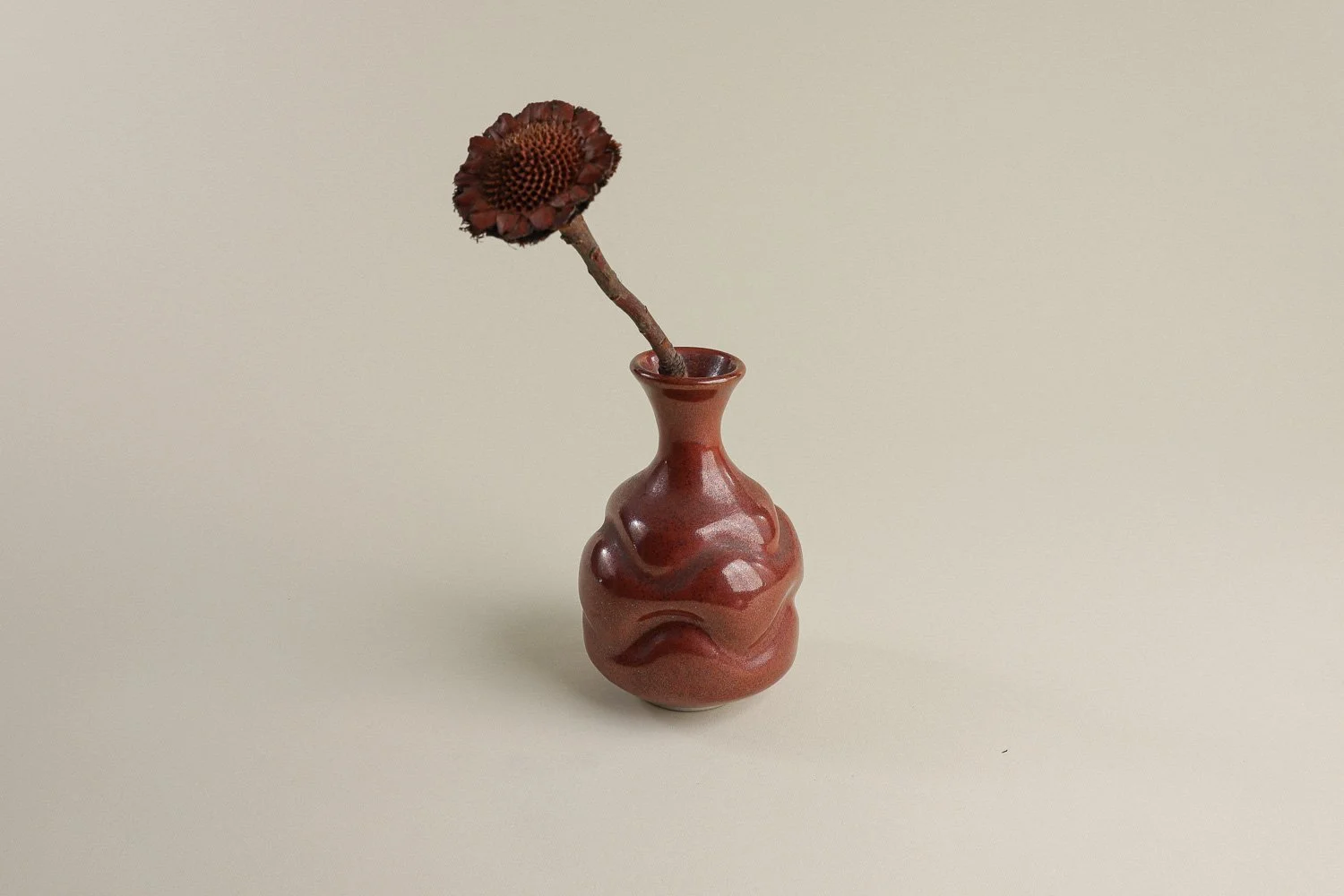 Handmade studio pottery bud vase featuring an organic, flowing form and reddish-brown glaze.