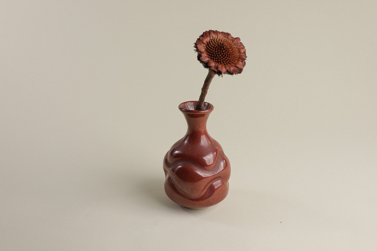 Handmade studio pottery bud vase featuring an organic, flowing form and reddish-brown glaze.