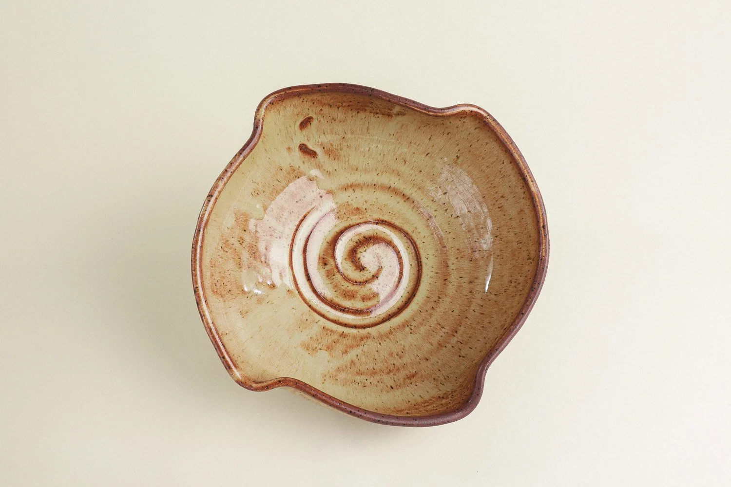 Handmade studio pottery bowl featuring a rustic, earthy-glazed swirl interior and a scalloped rim.