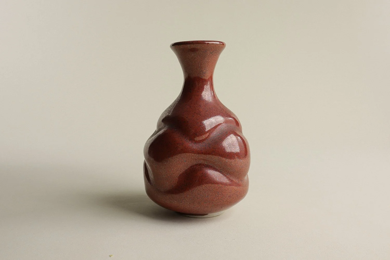 Handmade studio pottery bud vase featuring an organic, flowing form and reddish-brown glaze.